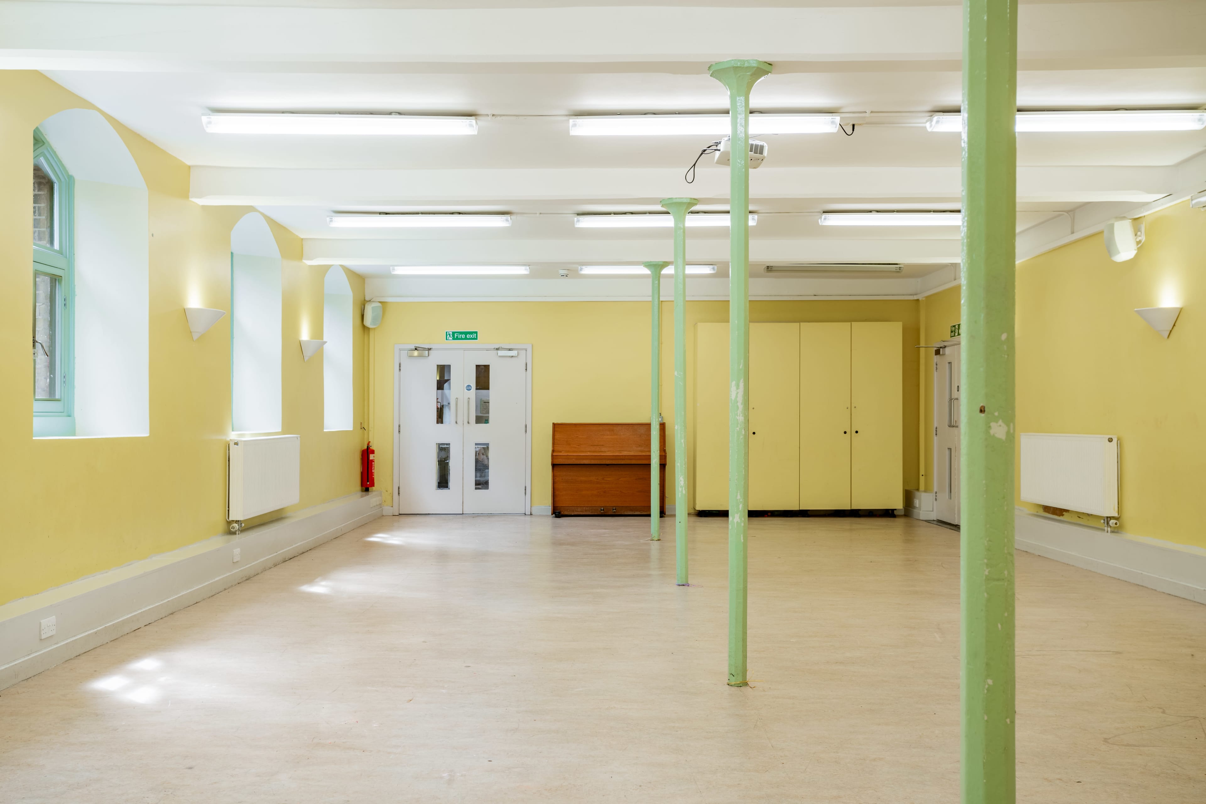 An empty room with yellow walls, fluorescent lighting, and green support columns.
