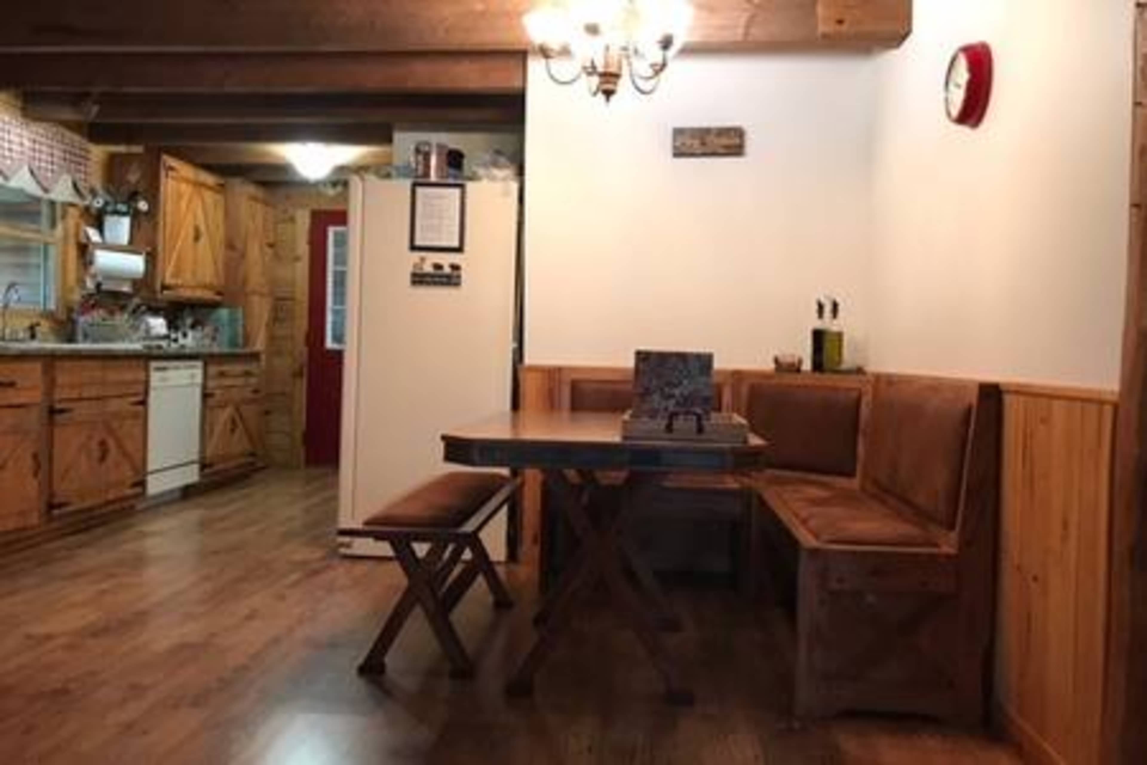 A wooden dining area features a round table and a bench, with a kitchen visible in the background.