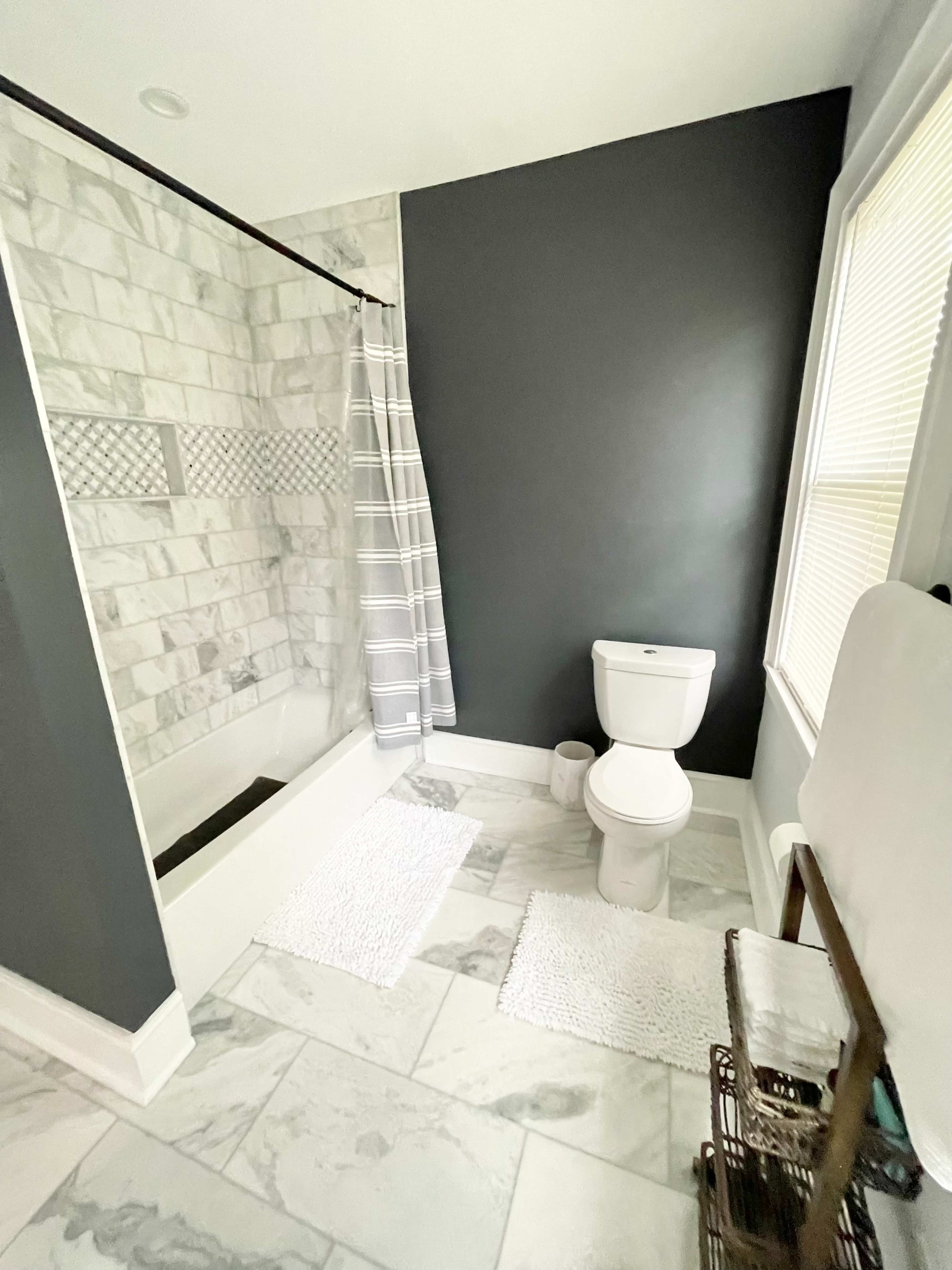 A modern bathroom features a tiled shower, a toilet, and two white rugs on a marble floor.