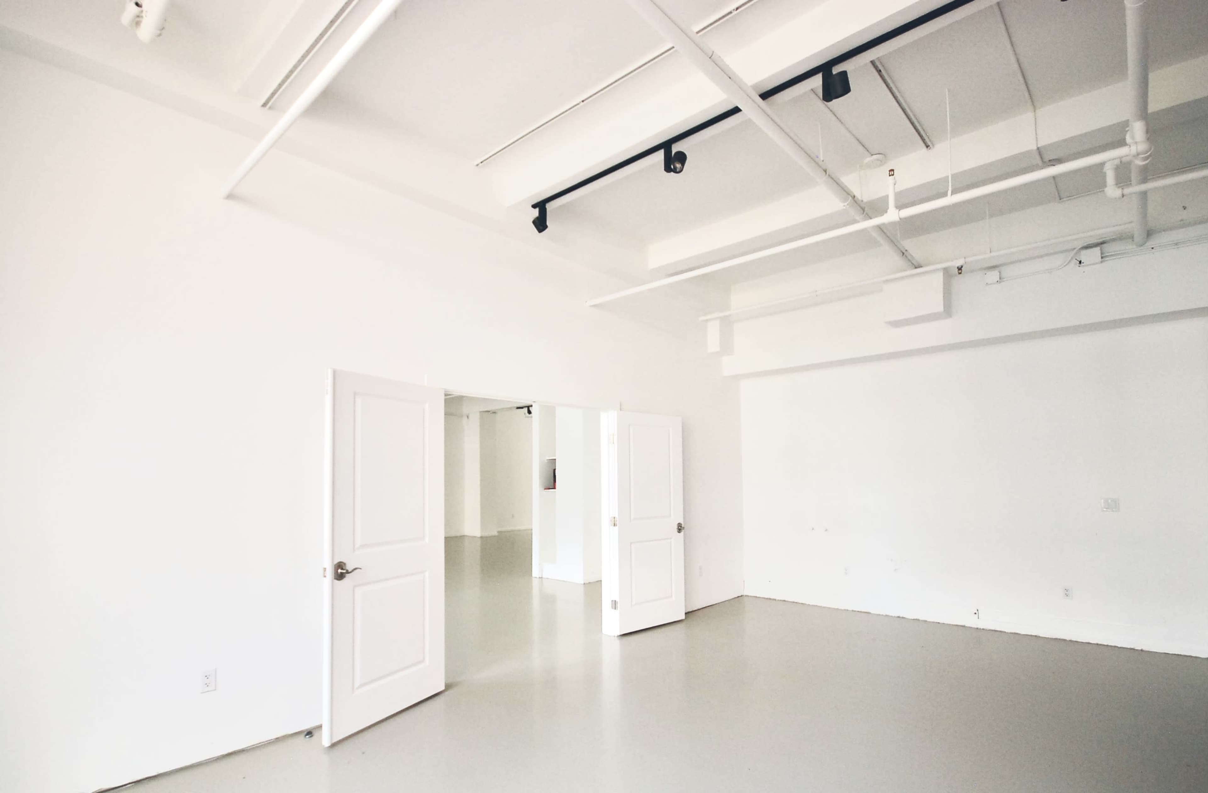 A wide, empty room with white walls, gray flooring, and two open doors leading to another space.