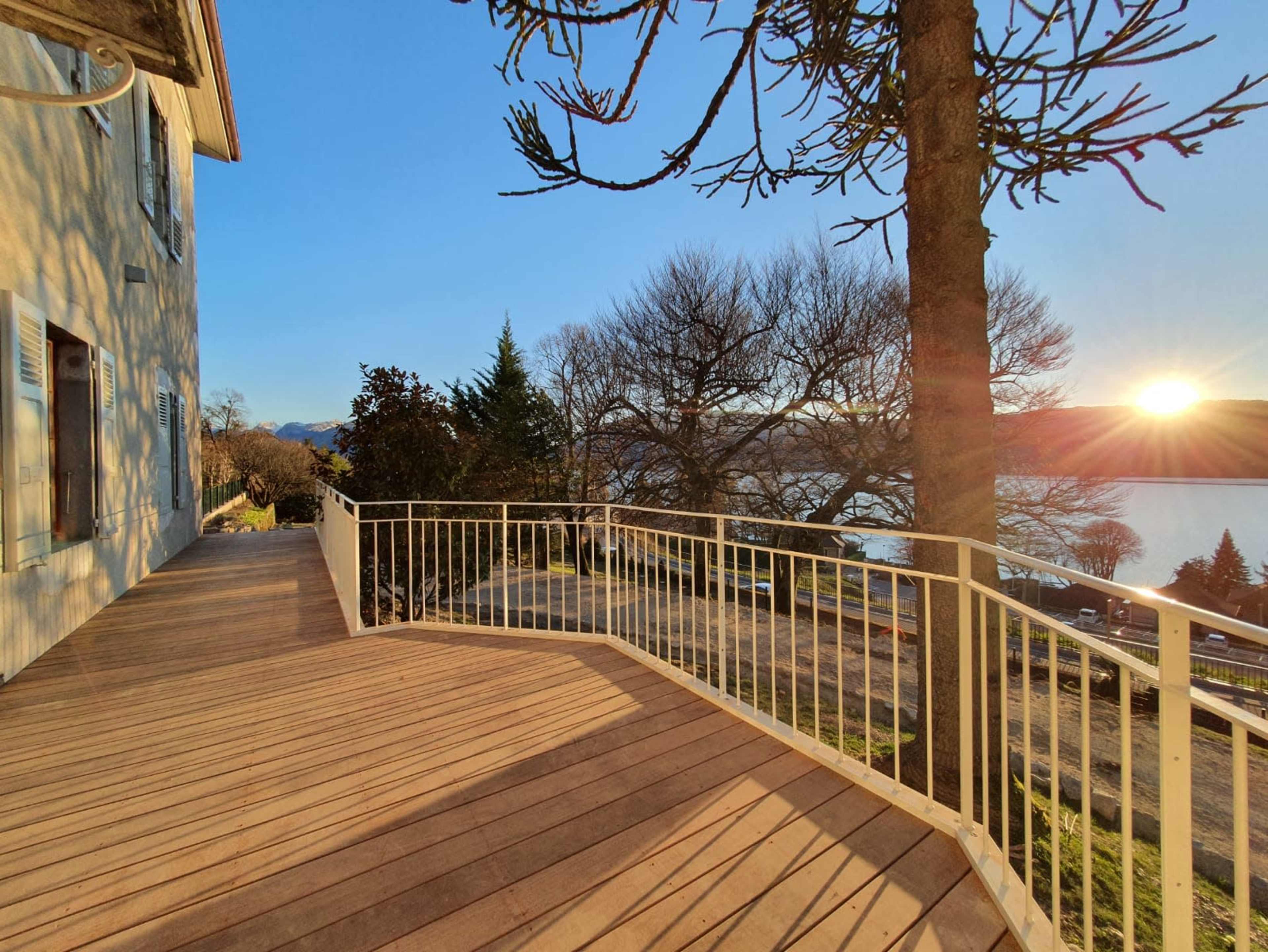 The image shows a wooden deck beside a lake, with a house on the left and a sunset visible in the background.