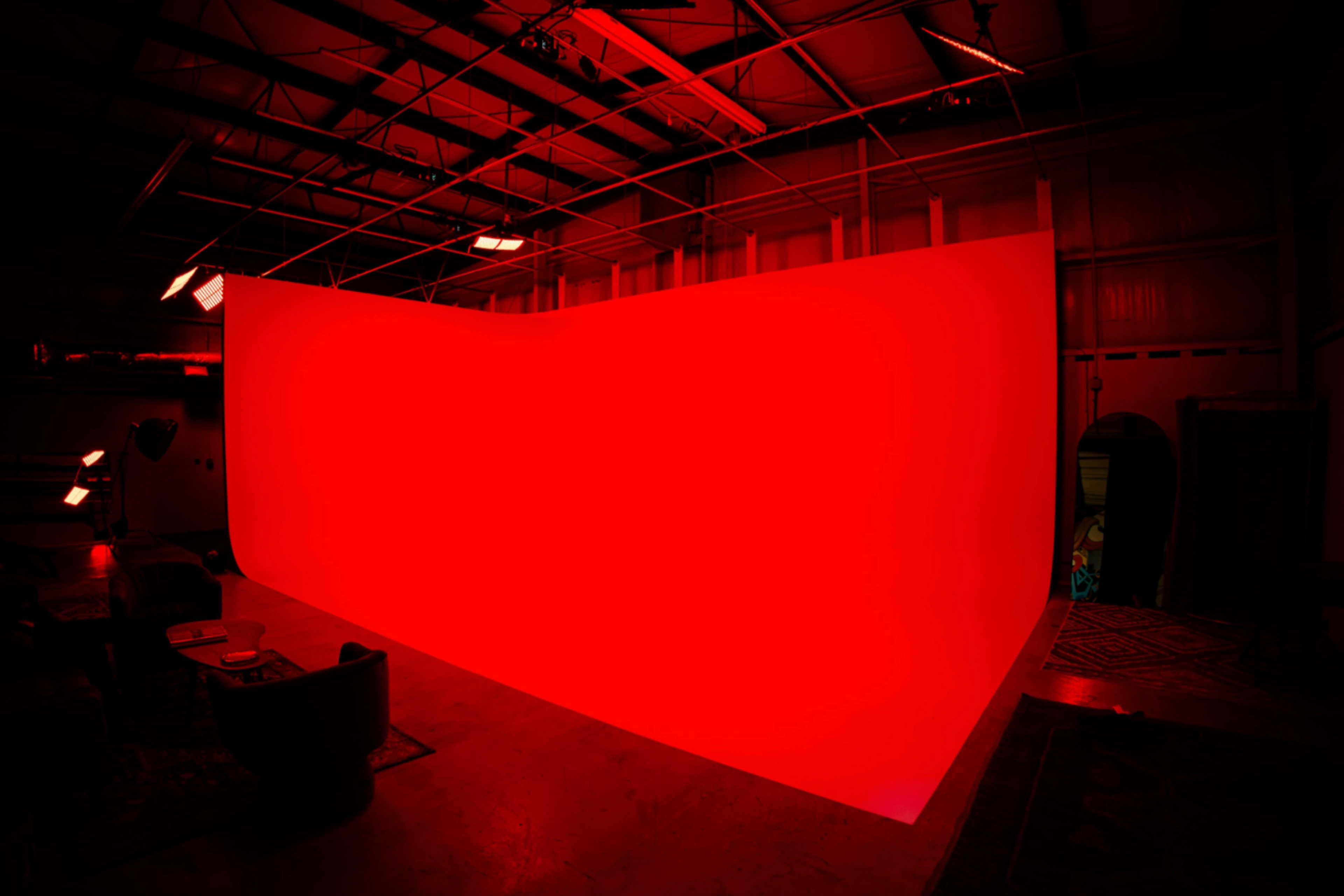 A large, curved red backdrop is set up in an industrial-style studio space with overhead lighting.