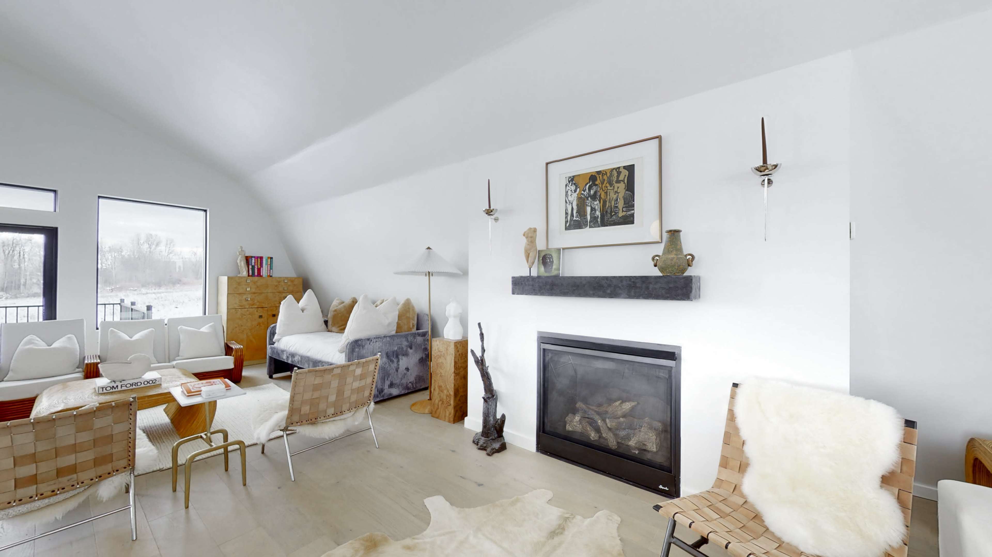 A modern living room with a minimalist design featuring a fireplace, art on the walls, and various seating arrangements.