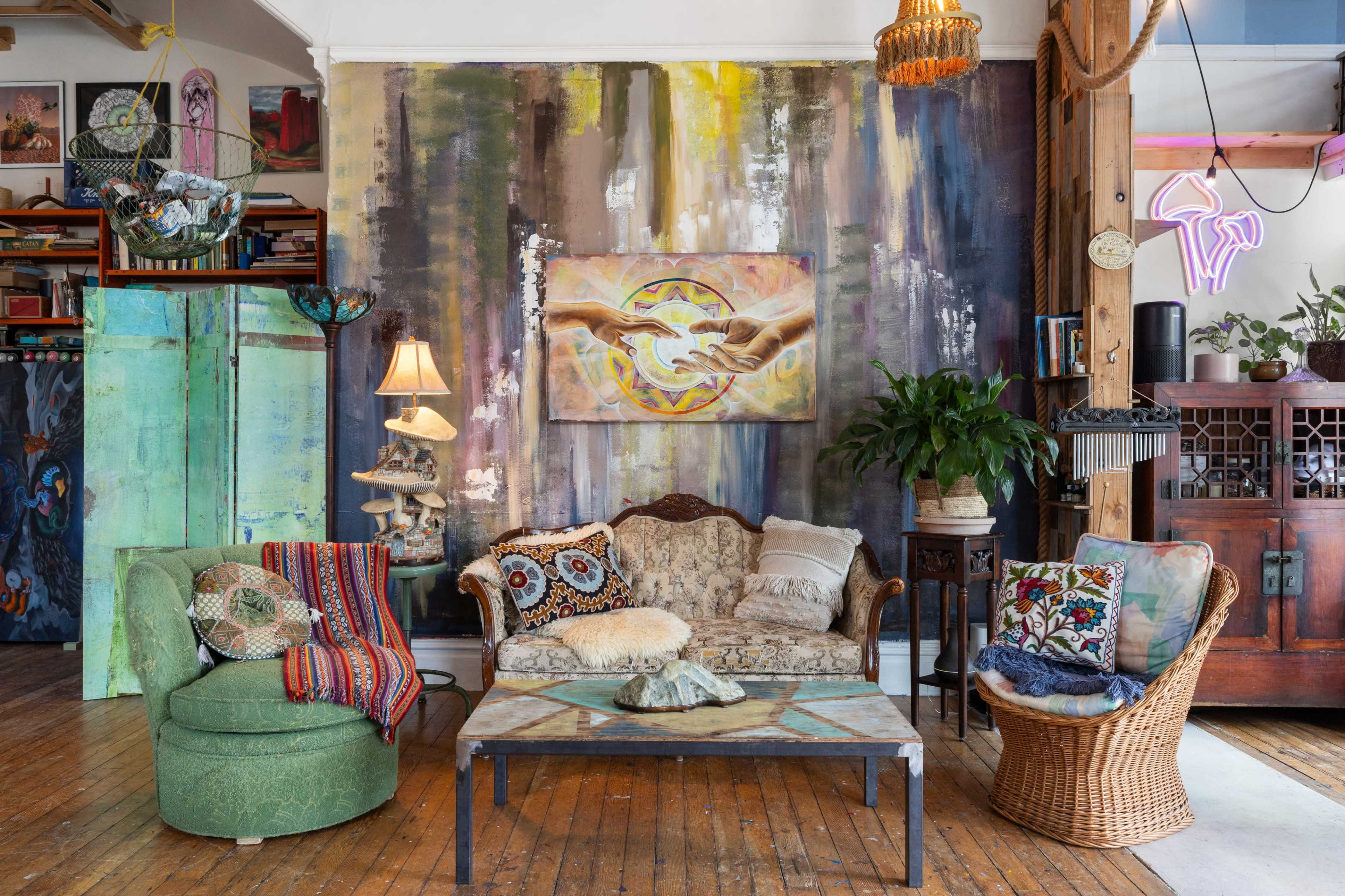 The image showcases a cozy living room with eclectic decor, featuring a patterned sofa, a wicker chair, a coffee table, and a large mural on the wall.