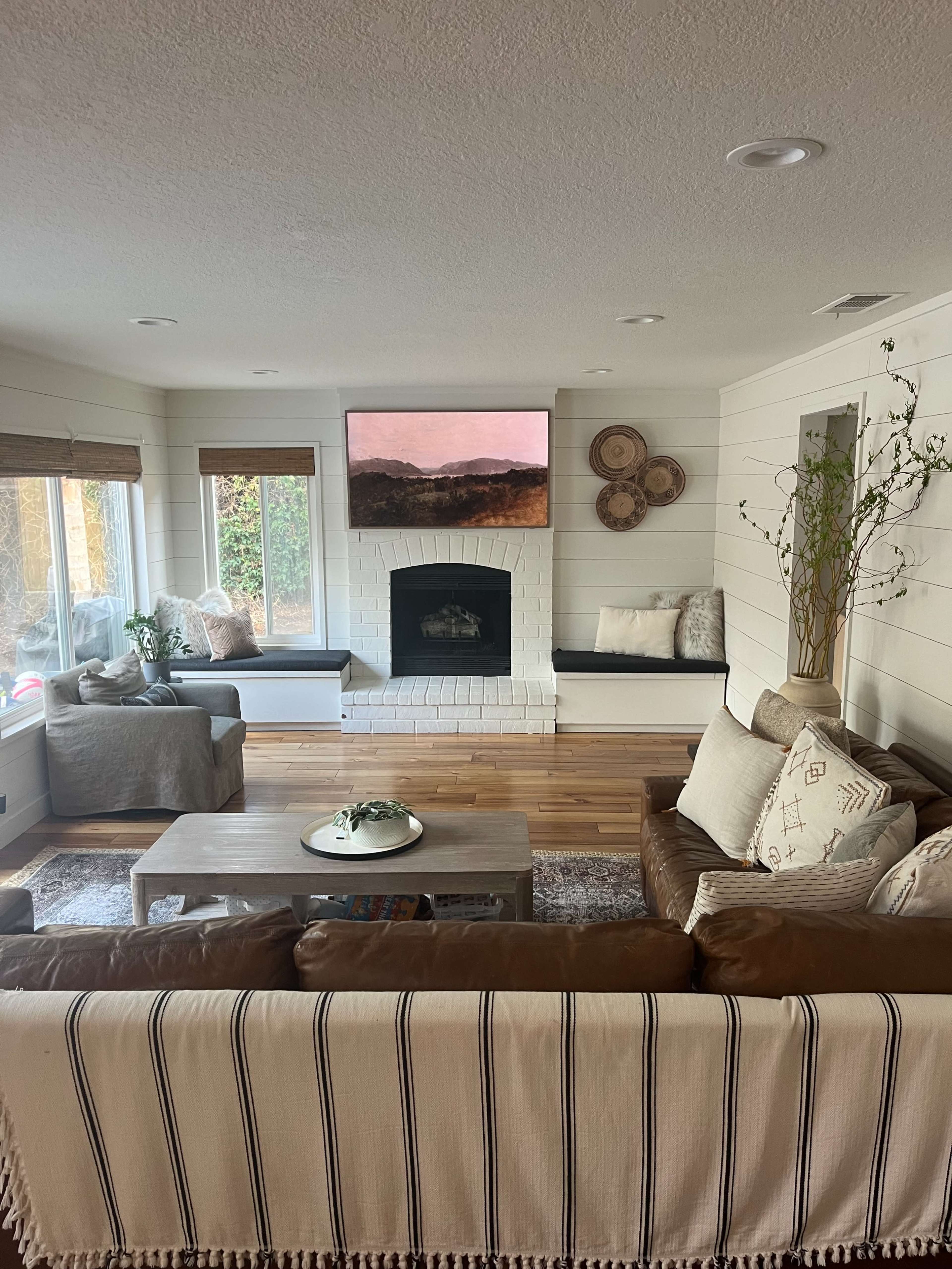 A well-lit living room features a fireplace, two benches, a coffee table, and a large wall-mounted artwork.