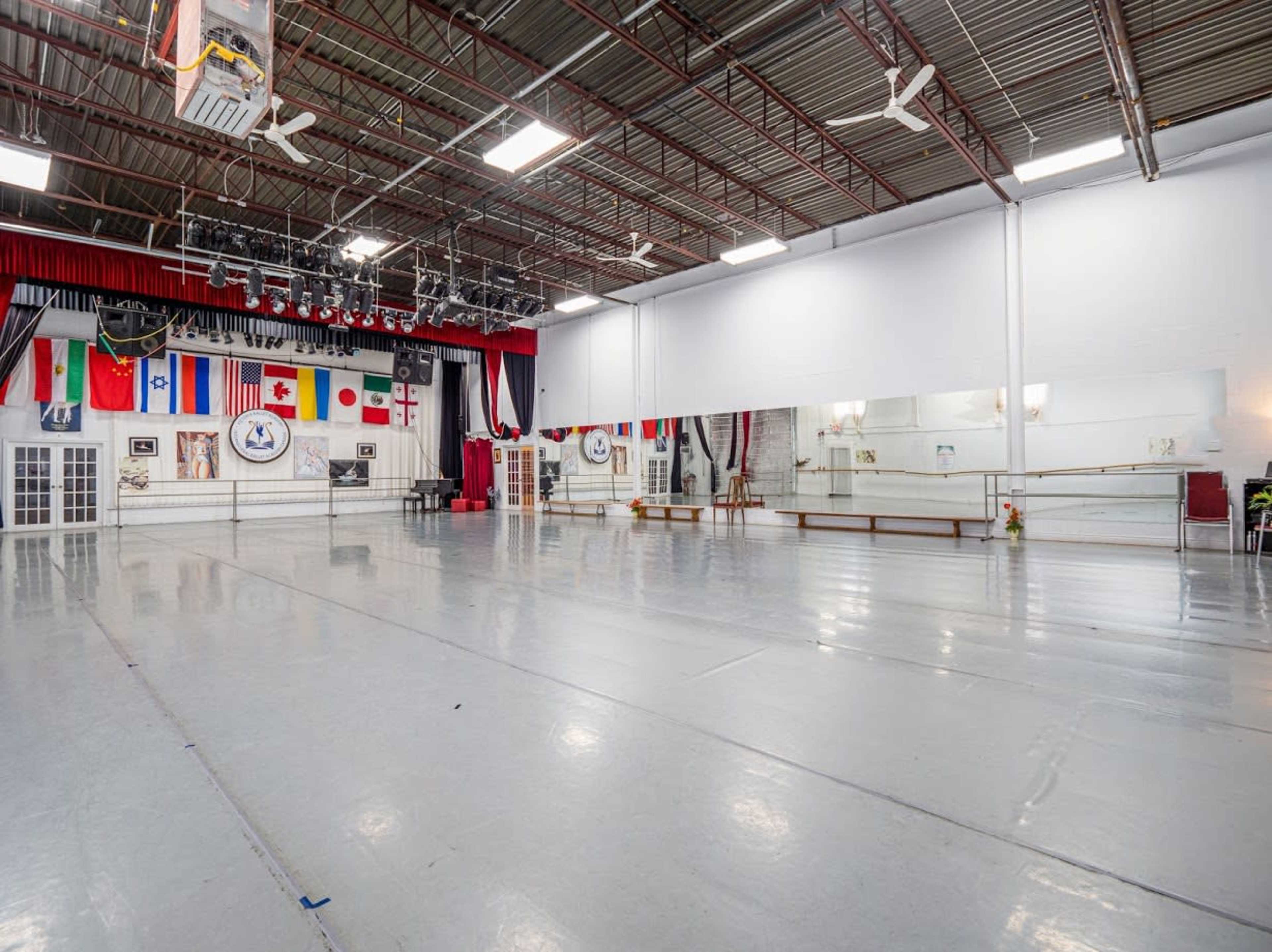 A spacious dance studio featuring a mirrored wall, ballet barre, and various flags displayed on the wall.