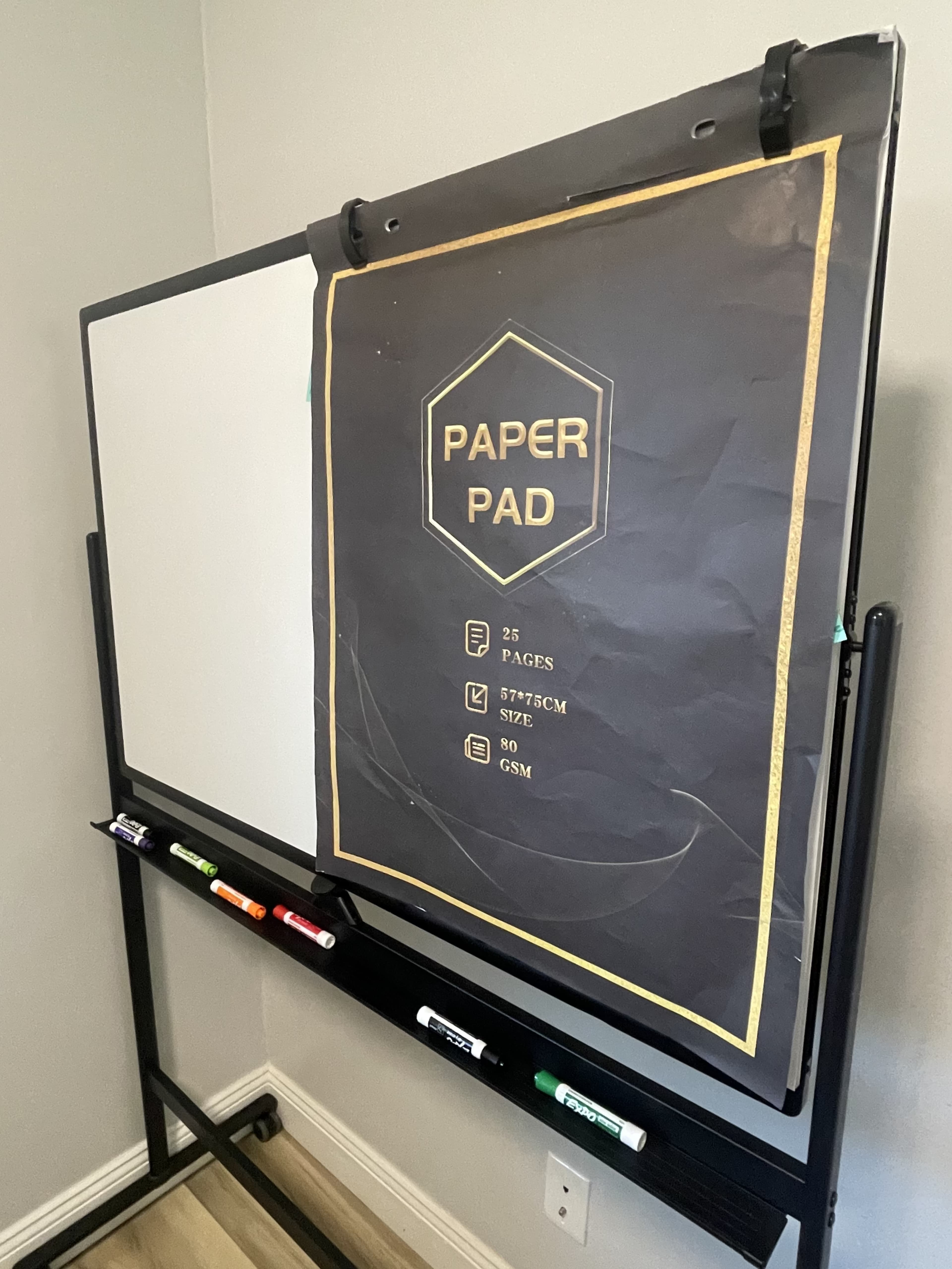 A large presentation board with a flip chart titled "Paper Pad" is mounted on a black stand, displaying details about its size and pages.