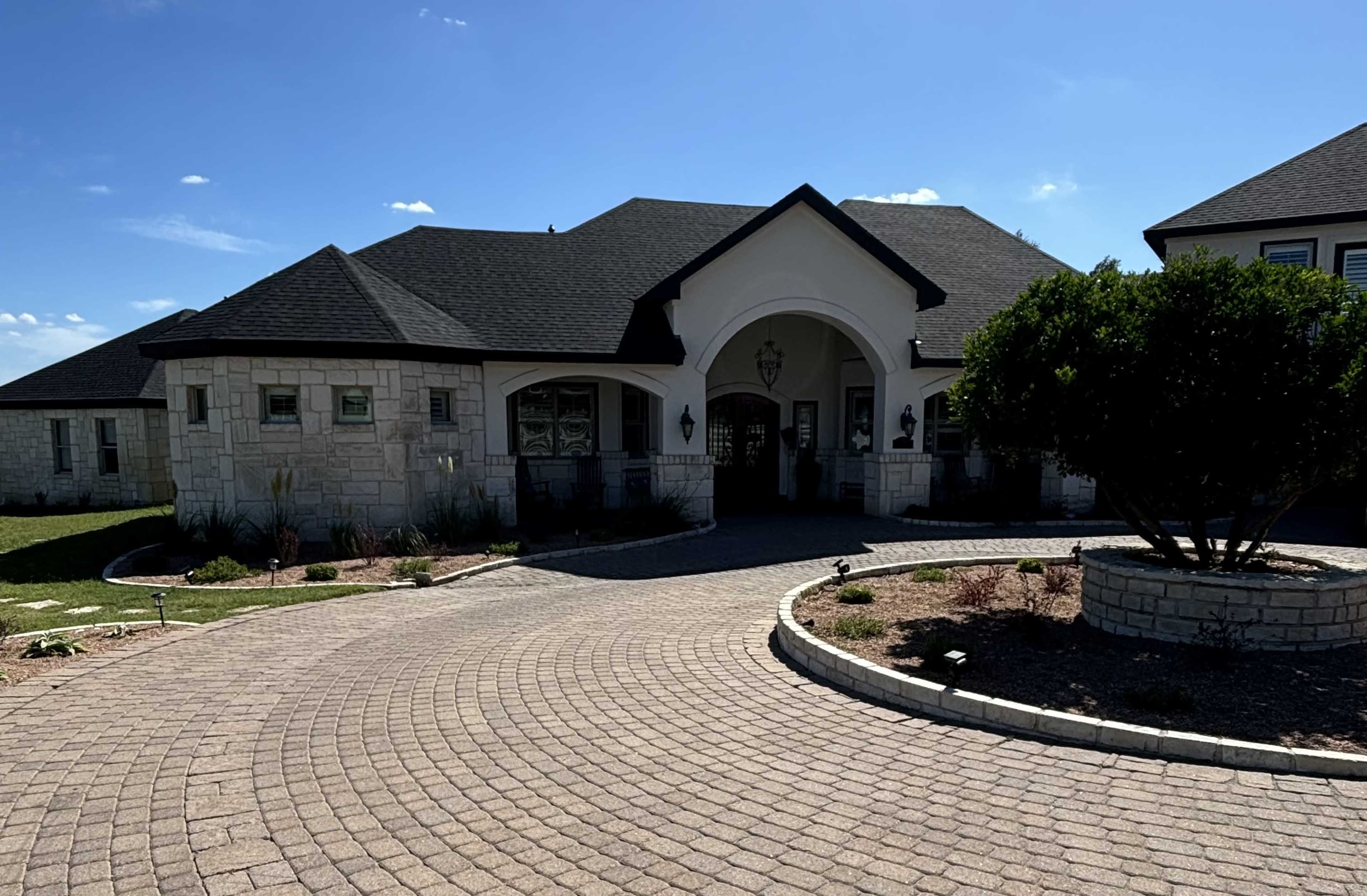 A sprawling single-story house with a curved entrance, surrounded by a paved driveway and landscaped areas.
