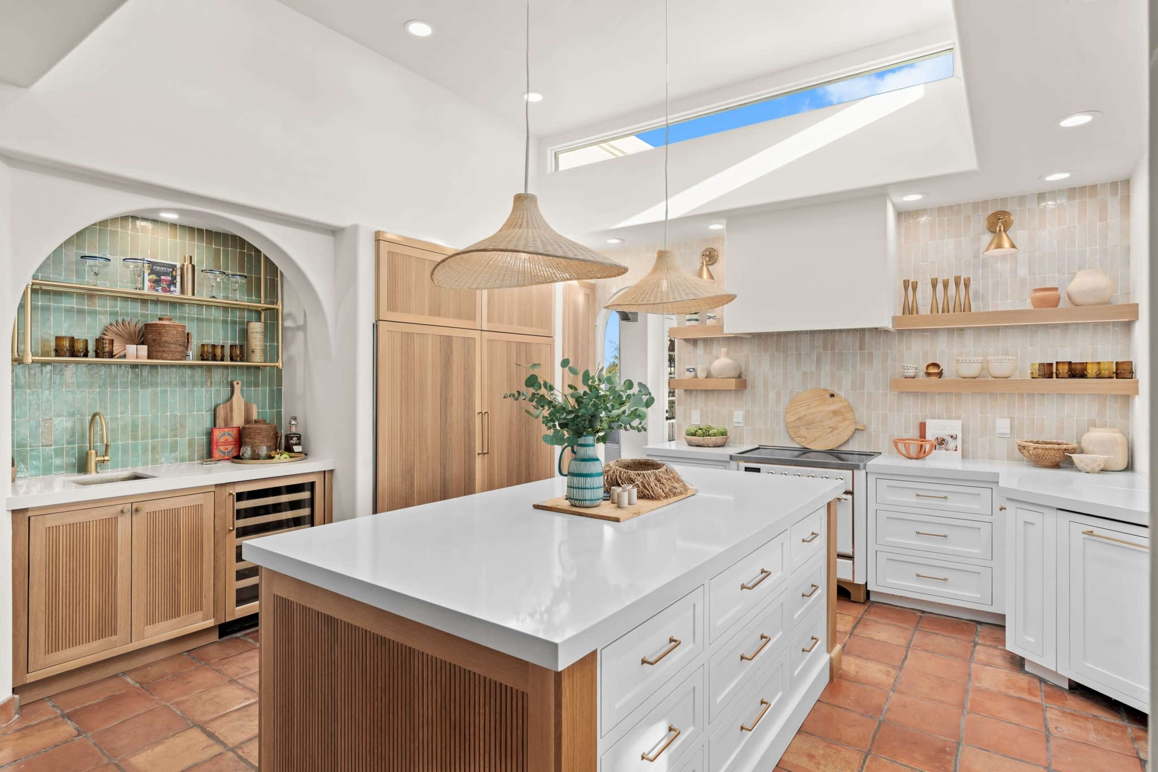 A modern kitchen features a central island with white countertops, wooden cabinetry, and an array of decorative items along the shelves and countertops.