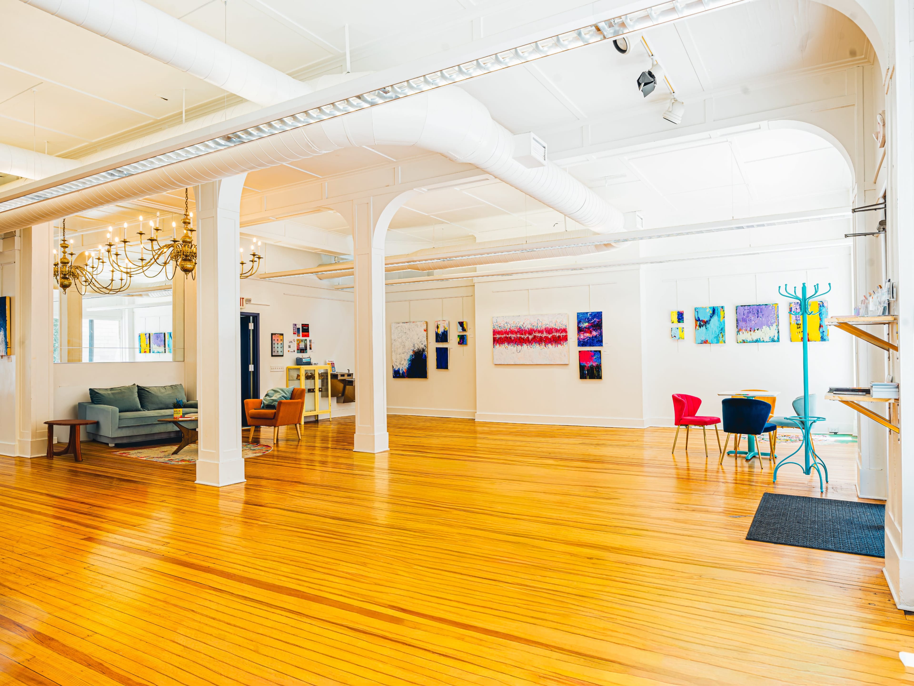The spacious room features wooden floors, large artwork on the walls, and various seating arrangements, including colorful chairs and a sofa.