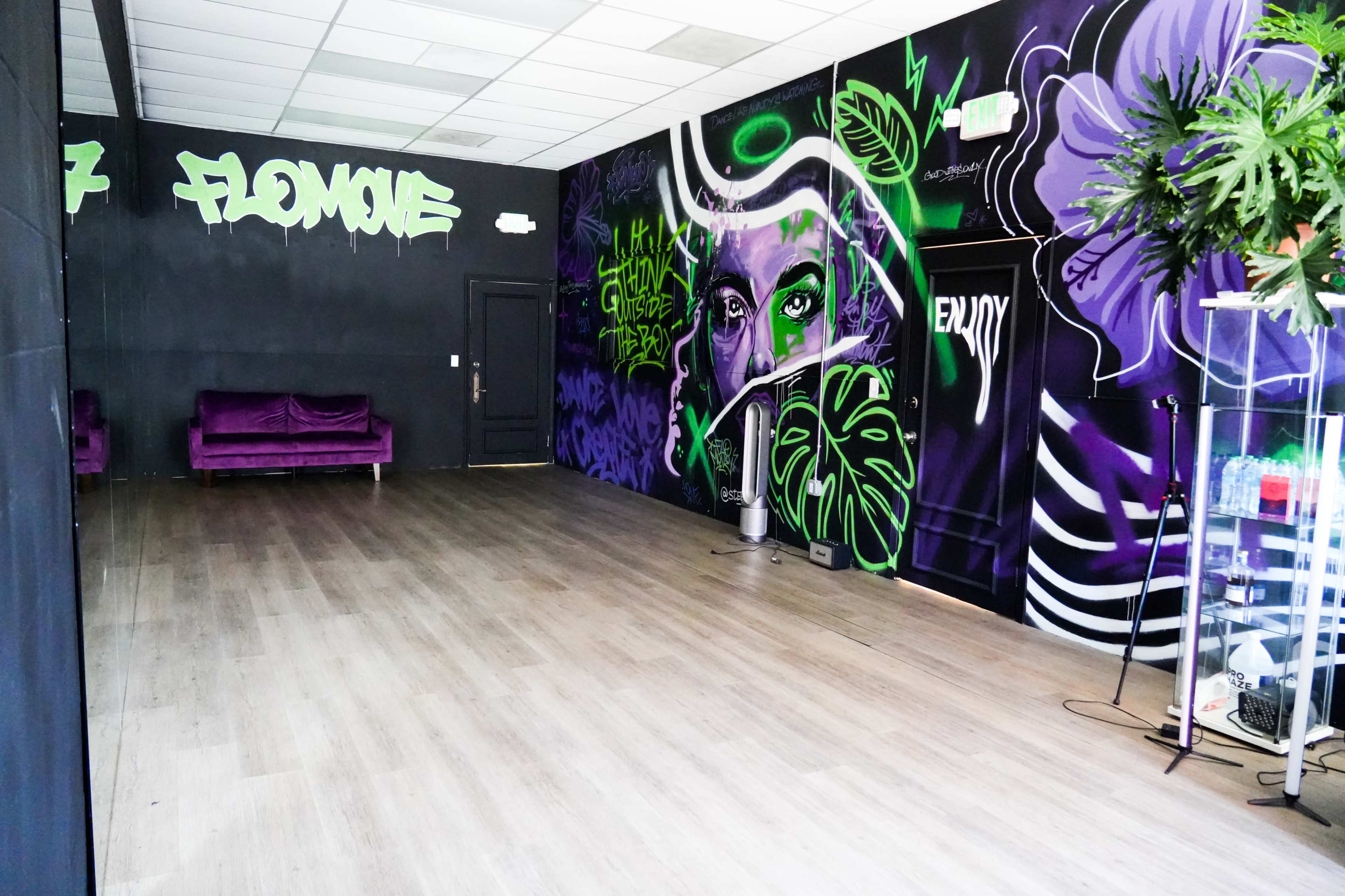 The image shows an empty room with dark walls featuring vibrant graffiti art, a purple couch on one side, and a glass display cabinet.