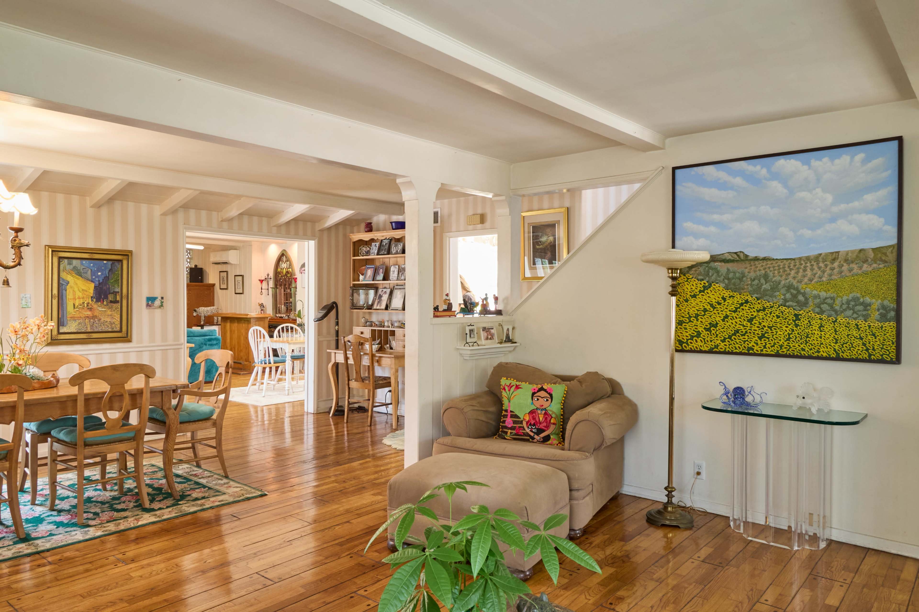 The image shows a cozy living space with wooden floors, a comfortable couch, and a dining area adjacent to it, decorated with plants and artwork.