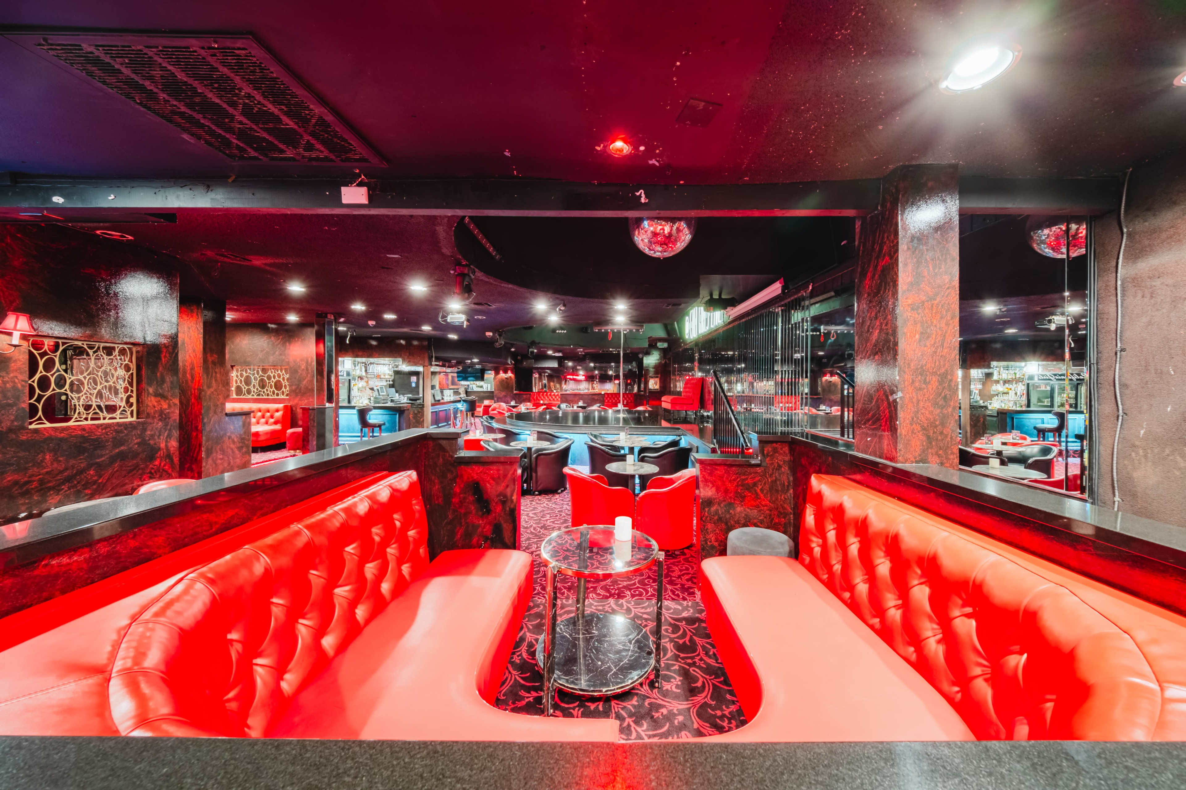 The image shows a dimly lit lounge with red upholstered seating, black accents, and mirrored walls.