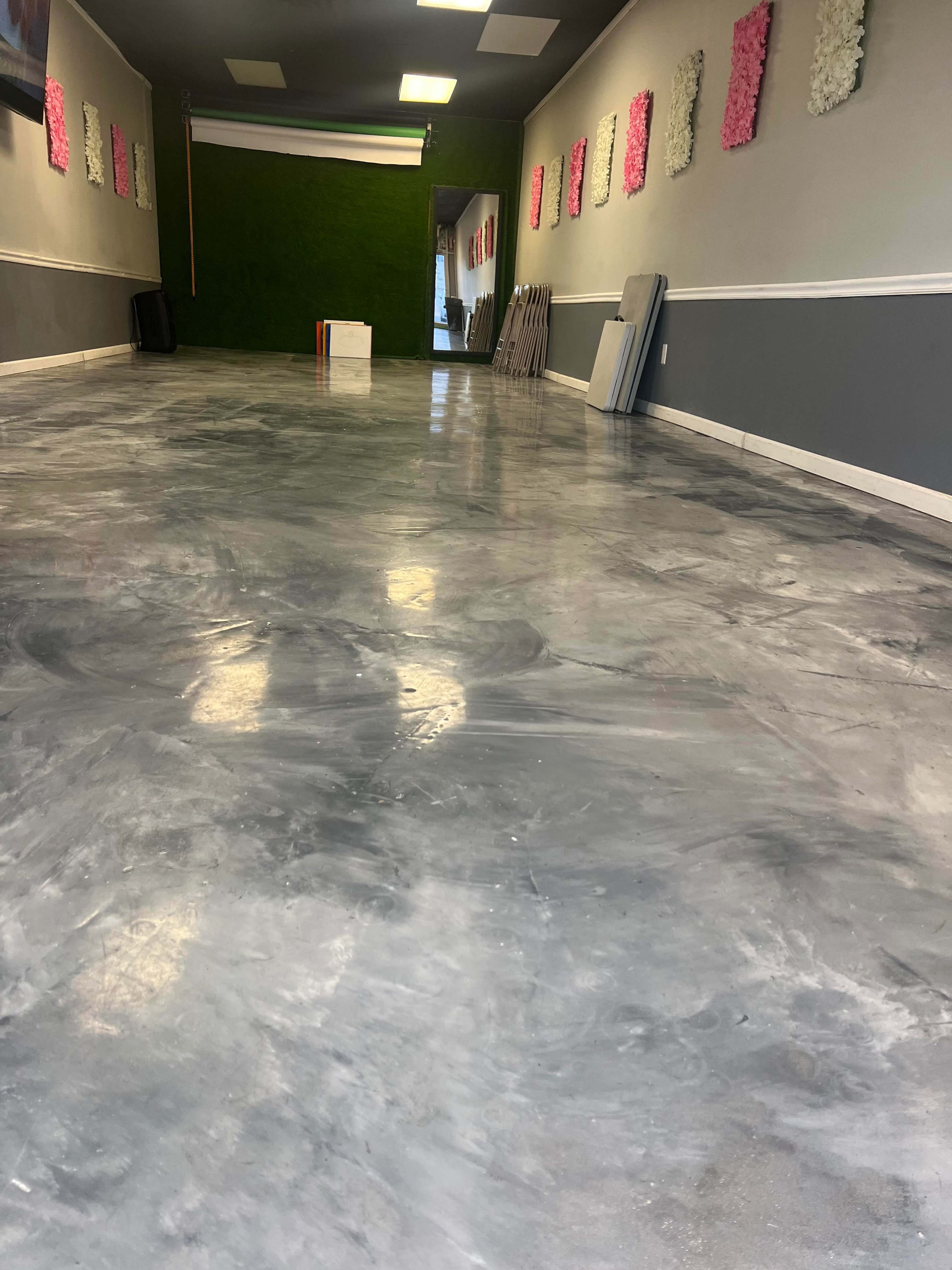 A spacious room with polished gray concrete flooring, green and pink wall decorations, and a doorway at the far end.
