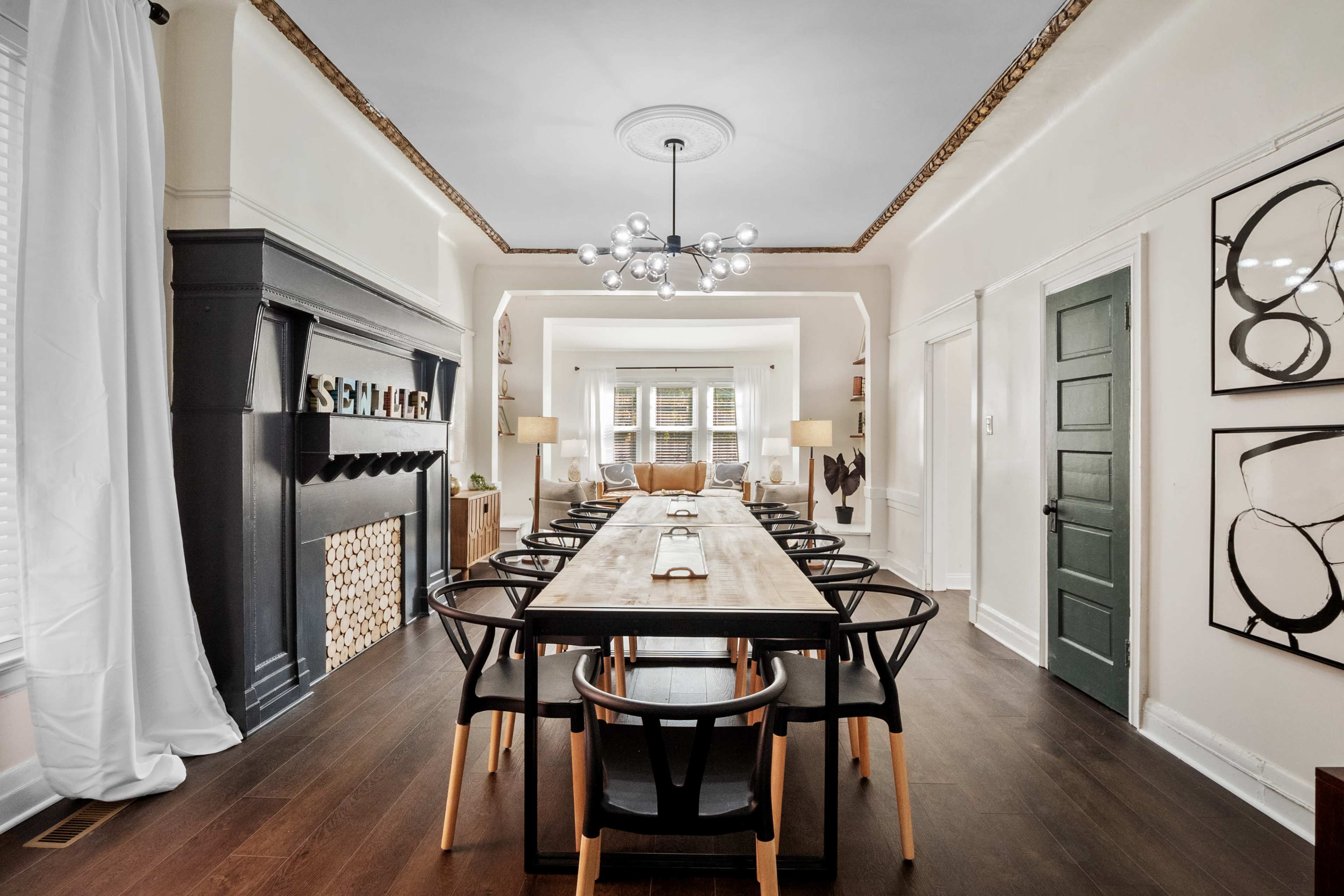 A long dining table with black chairs is set in a stylish room featuring a fireplace and large windows.