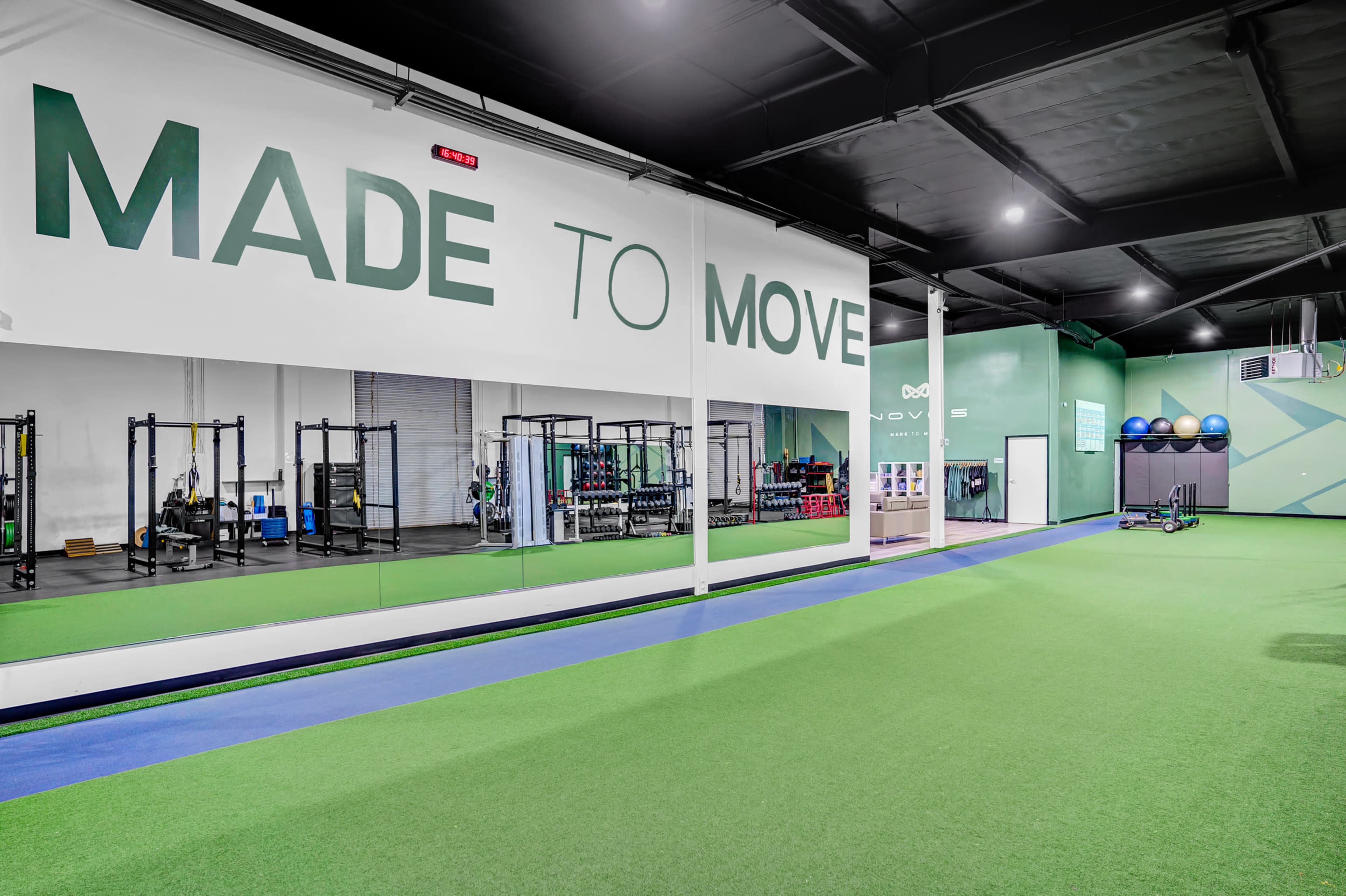 A fitness facility with green synthetic turf, strength training equipment visible in the background, and a large wall sign that reads "MADE TO MOVE."