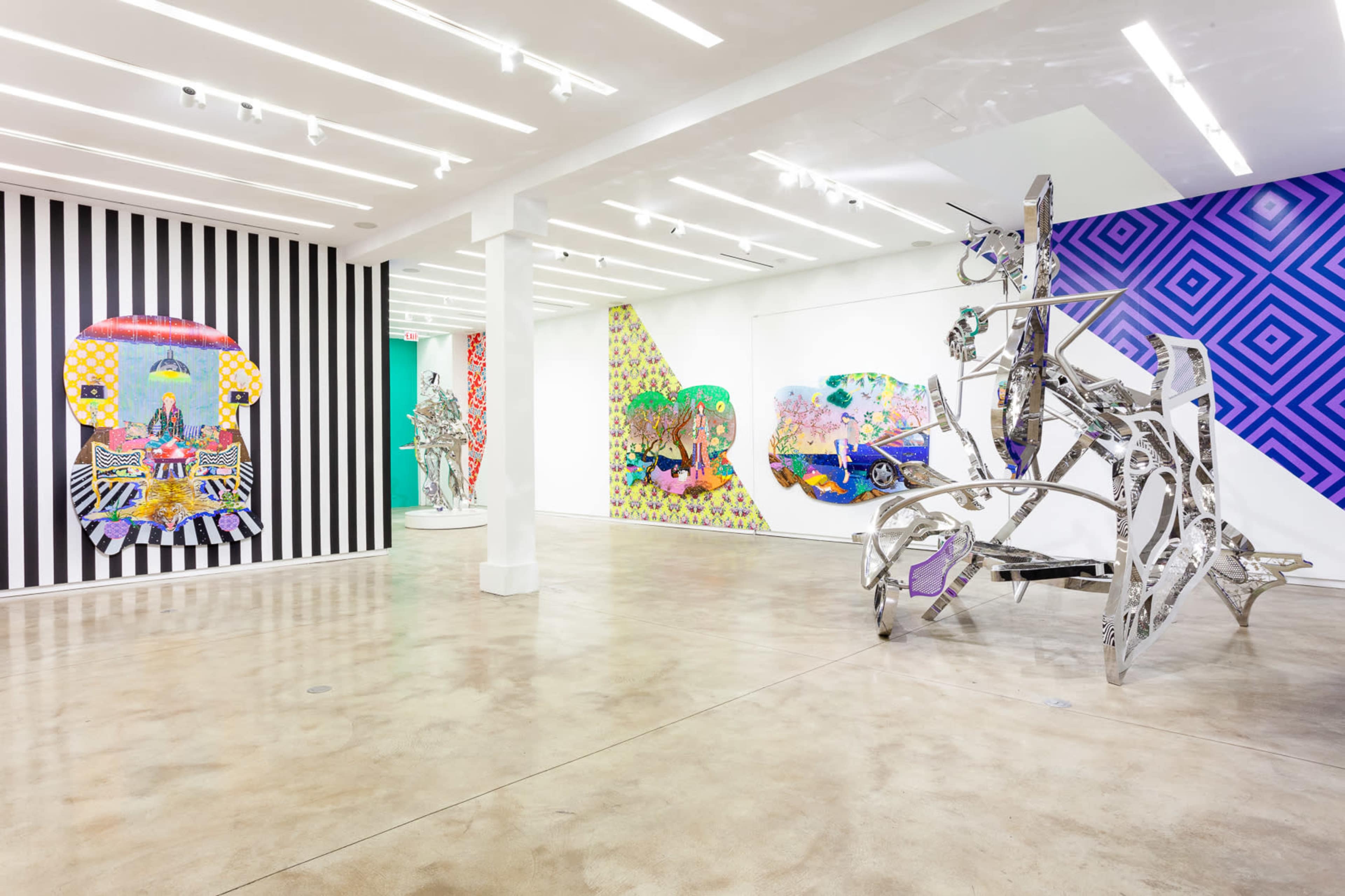 The image shows an art gallery featuring colorful wall murals and contemporary sculptures displayed across a bright, spacious room with modern lighting.