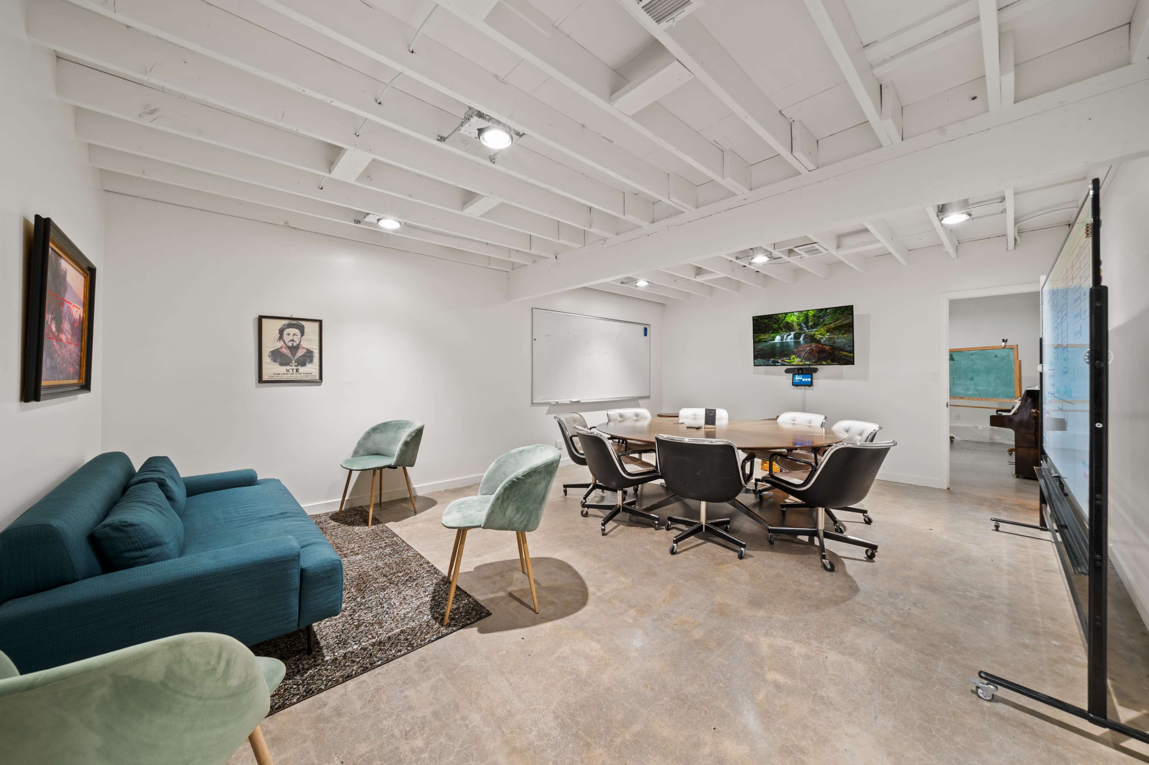 A conference room features a round table surrounded by black and white chairs, a whiteboard, and large screens on the walls.