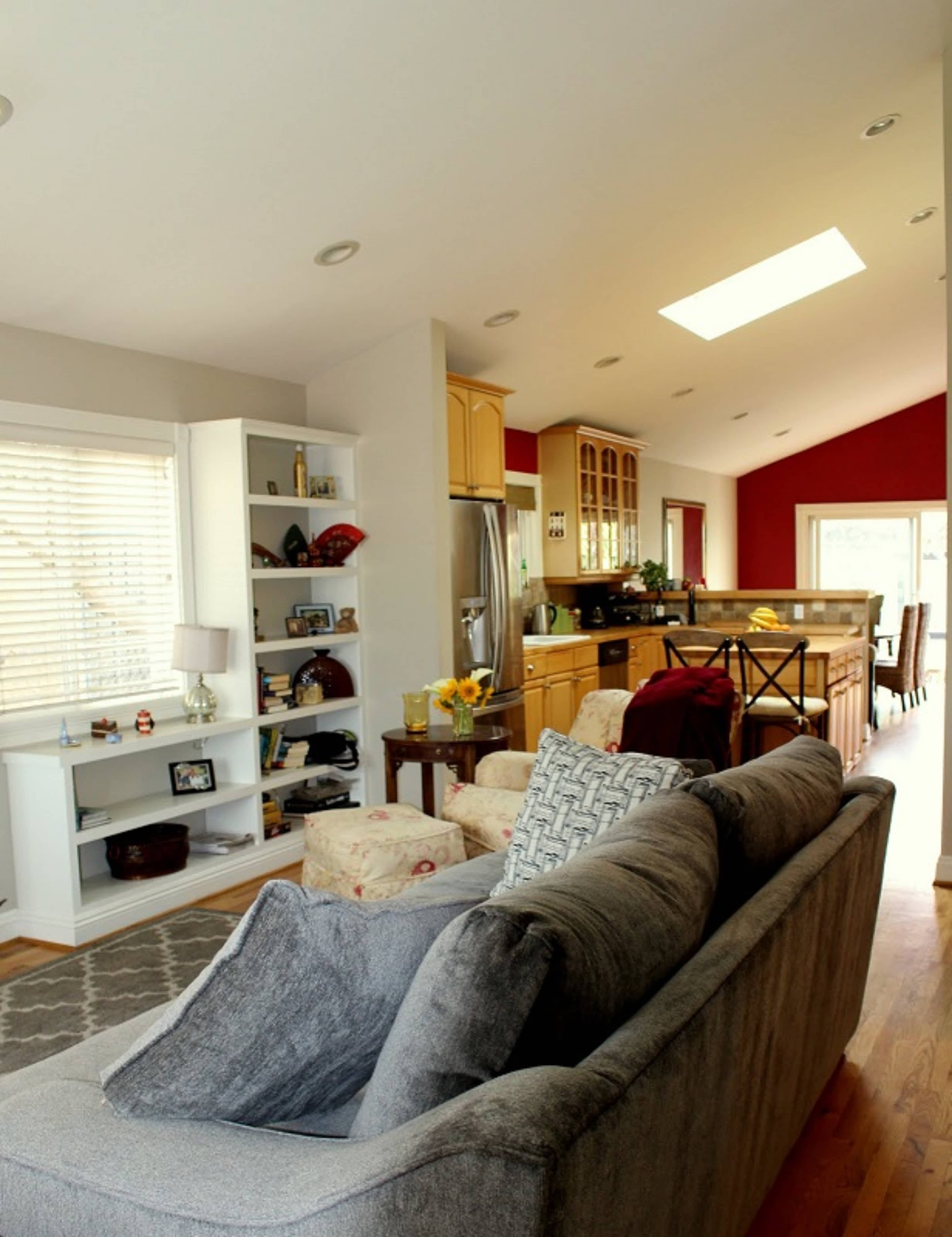 A spacious living area that opens into a kitchen, featuring a sectional couch, a dining table in the background, and large windows allowing natural light.