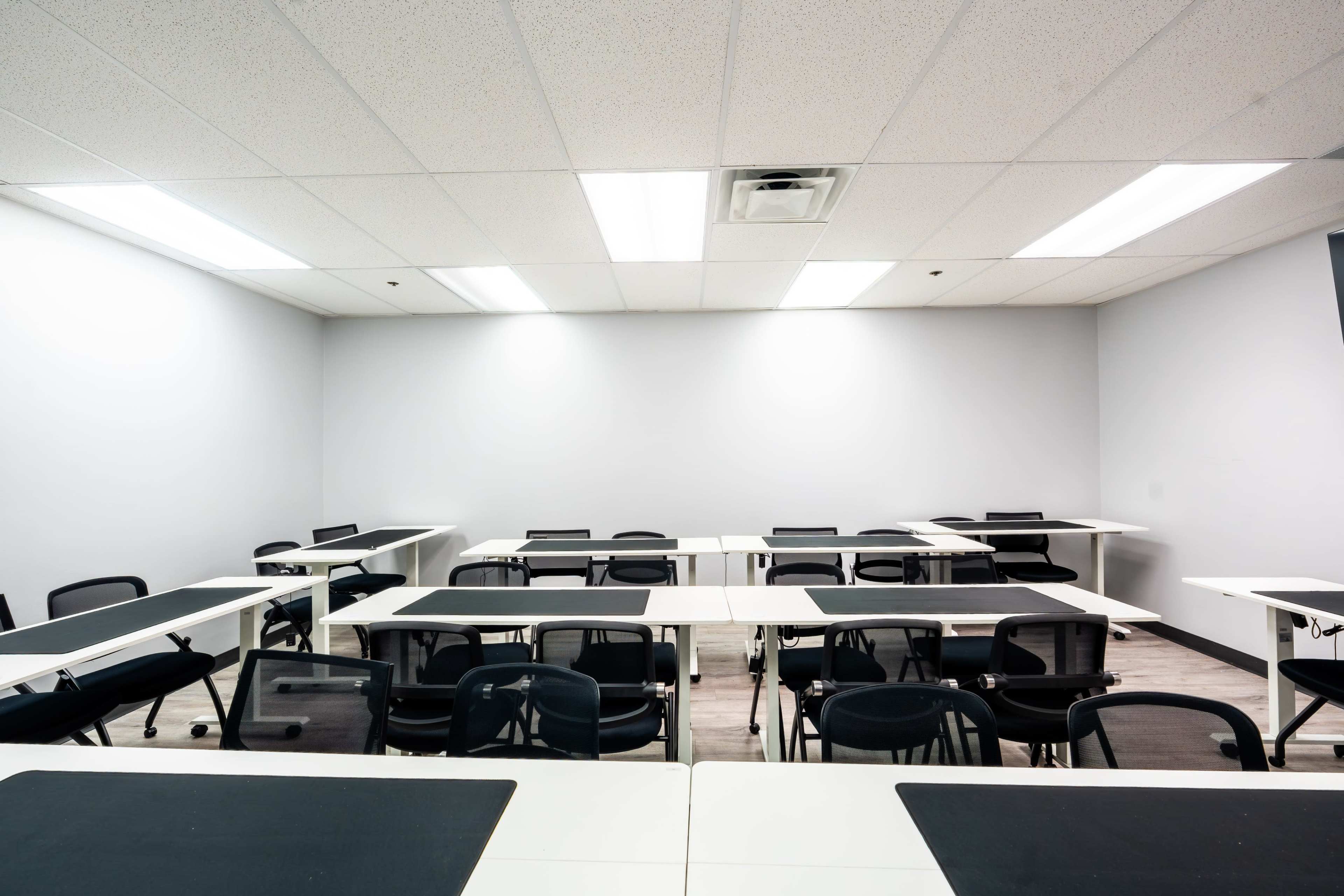 The image shows a classroom with several rows of tables and chairs arranged neatly in a bright, minimally decorated space.