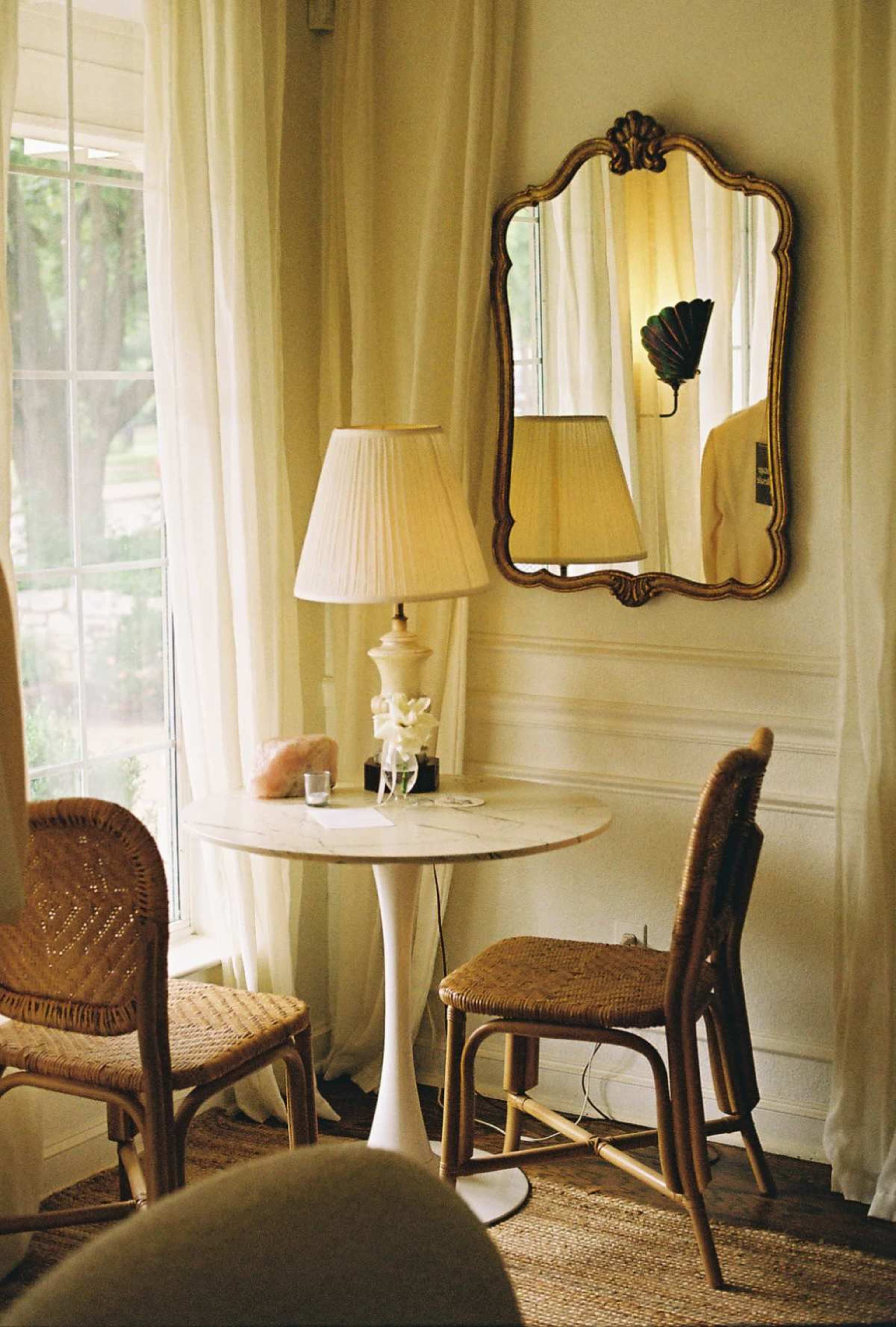 A small round table with two chairs is positioned near a window, featuring a lamp and a decorative mirror on the wall.