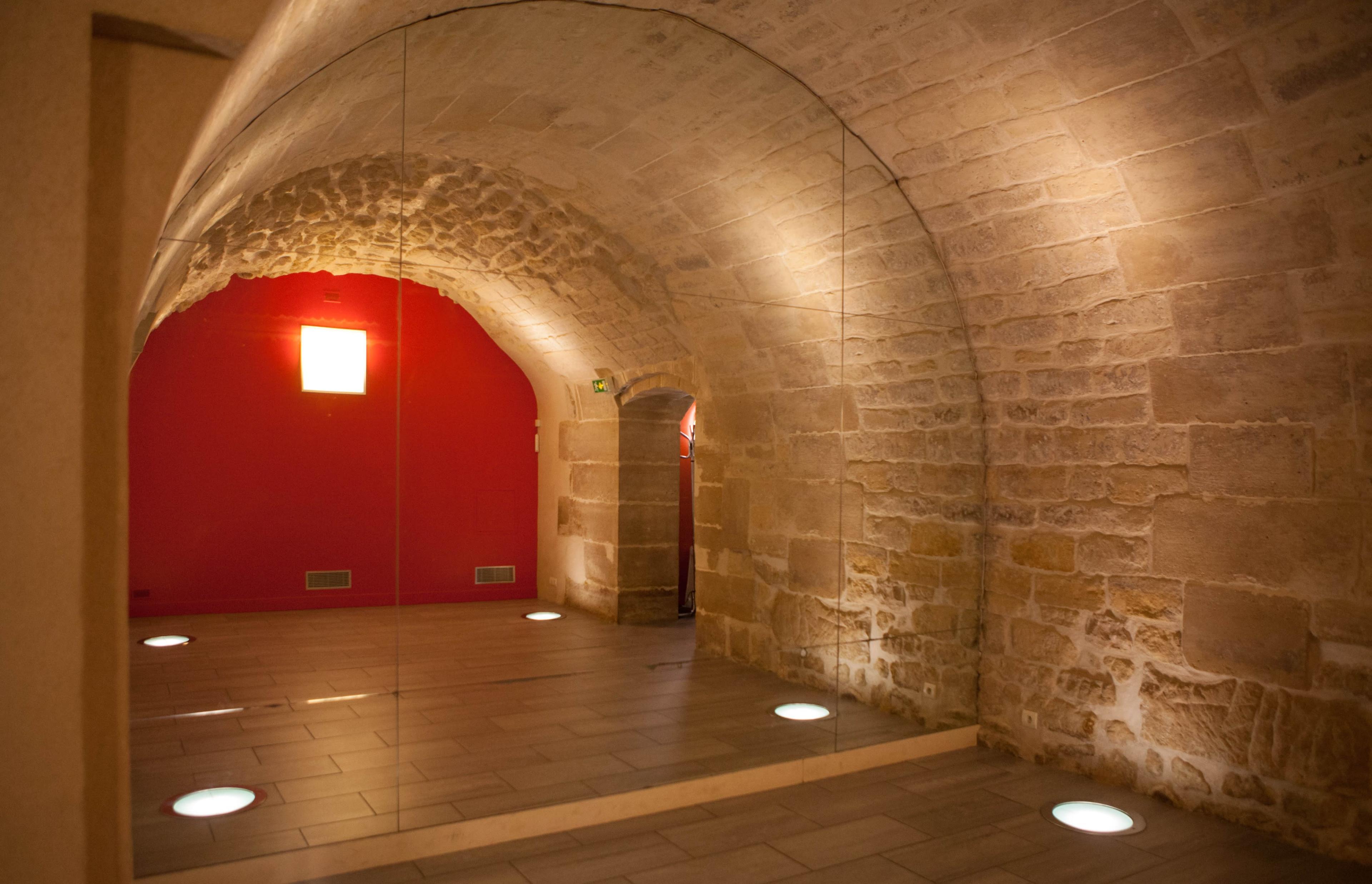 The image shows an arched stone room with a red wall and round floor lights illuminating the space.
