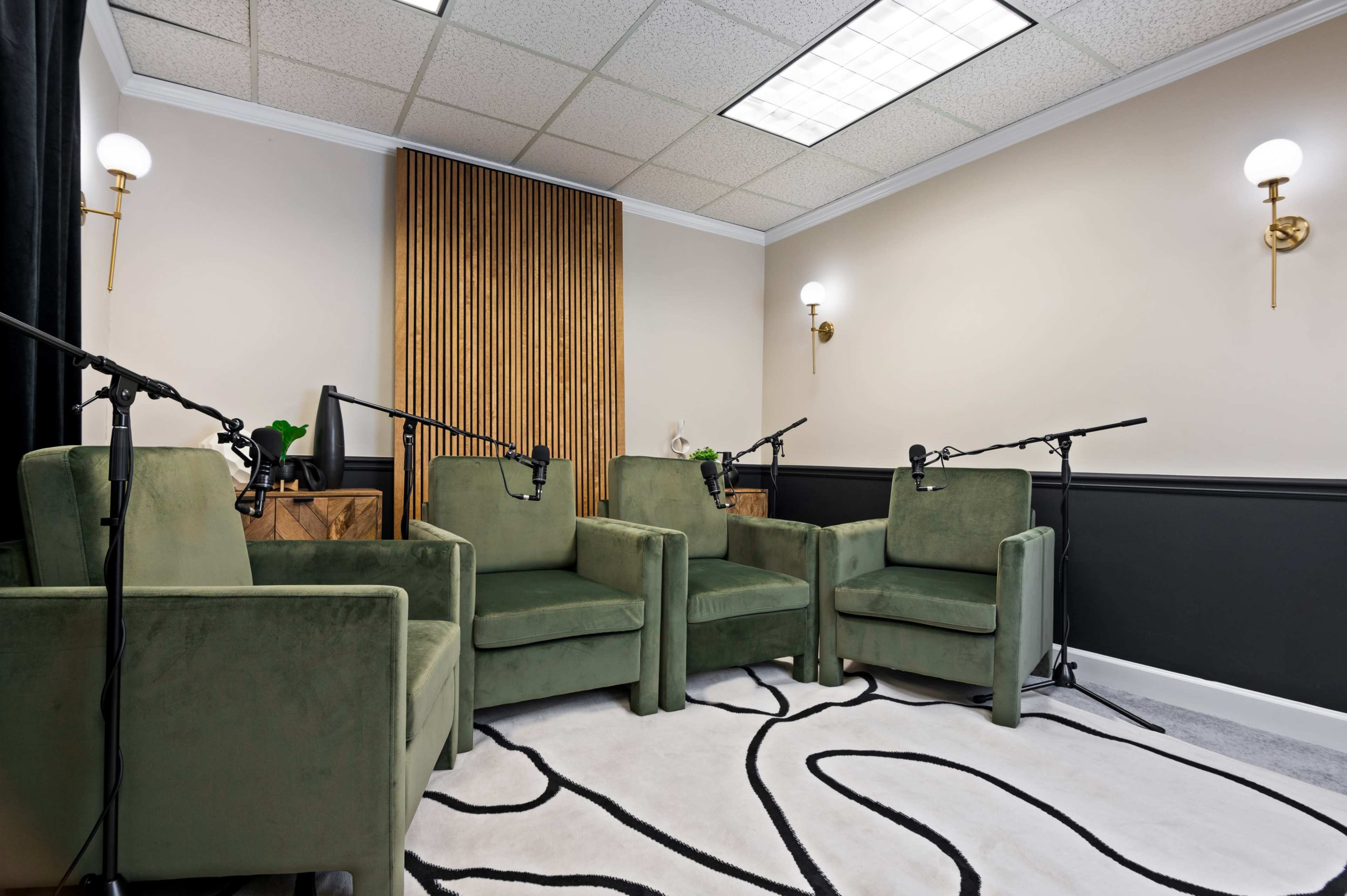 The image shows a small recording studio with four green chairs arranged around a carpet, each equipped with a microphone.