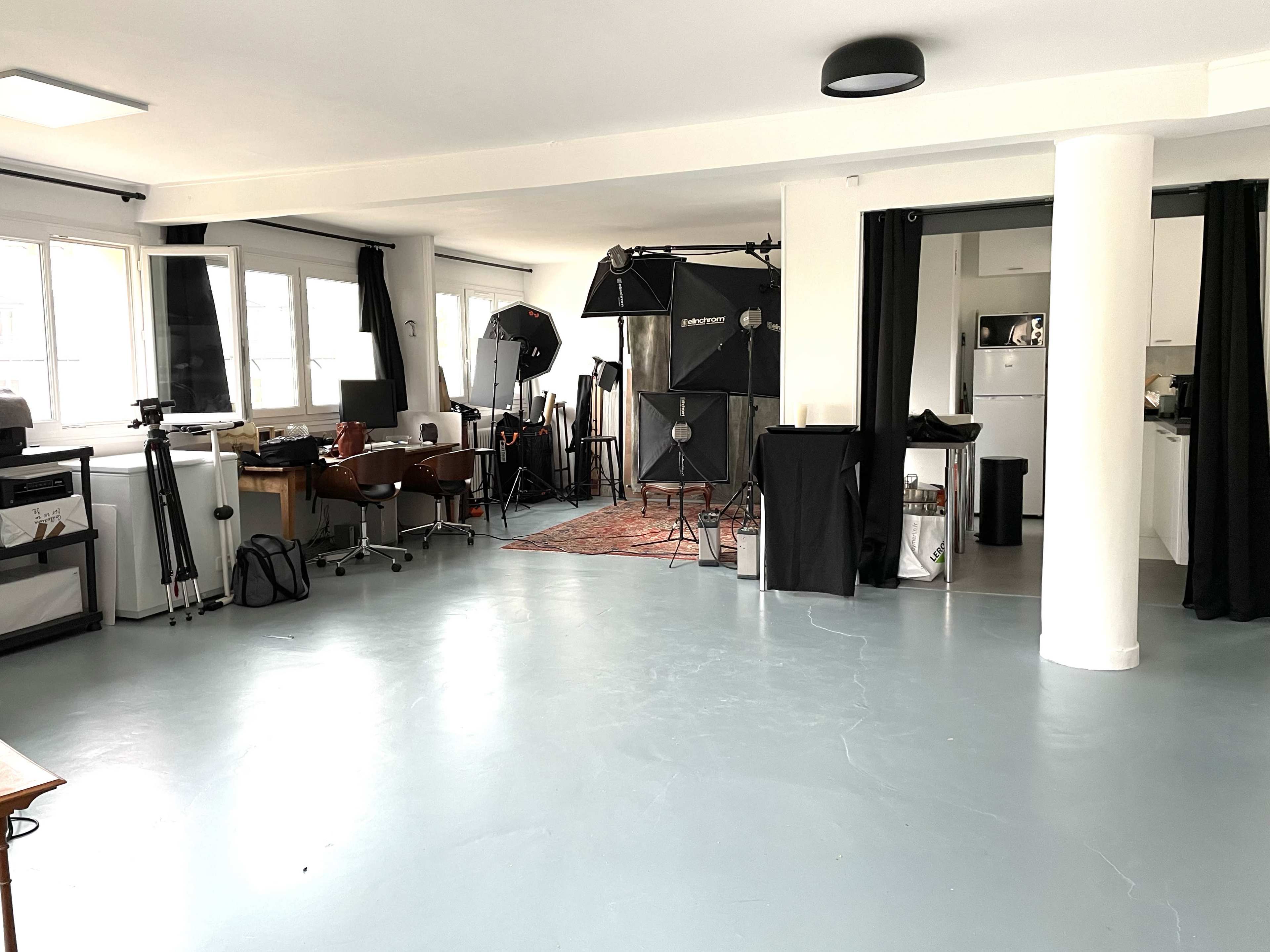 The image shows a spacious studio with photography equipment, including tripods and backdrops, and furniture for a work setup.