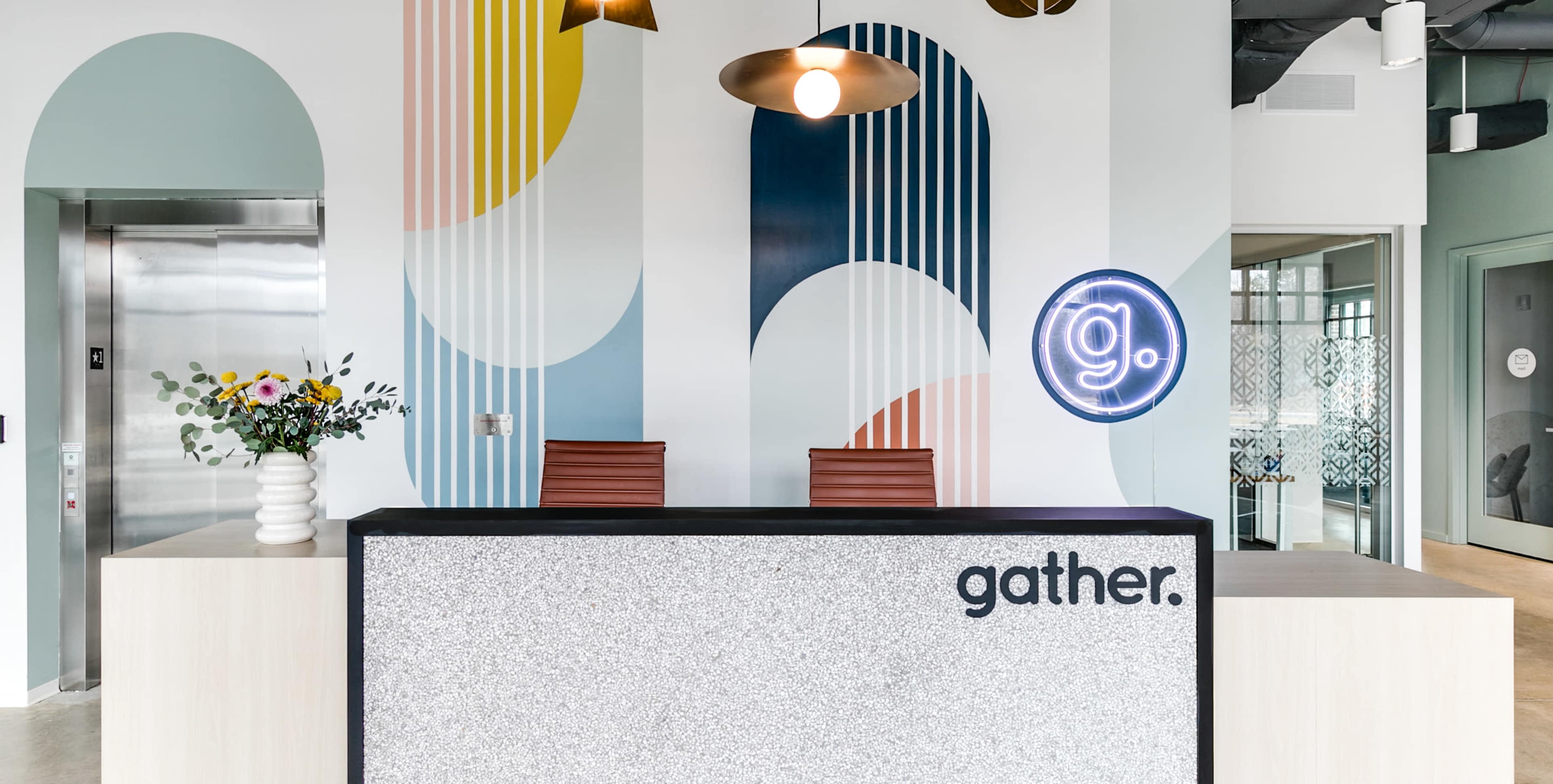A modern reception area with a patterned wall, a sleek front desk displaying the word "gather," and two wooden chairs.