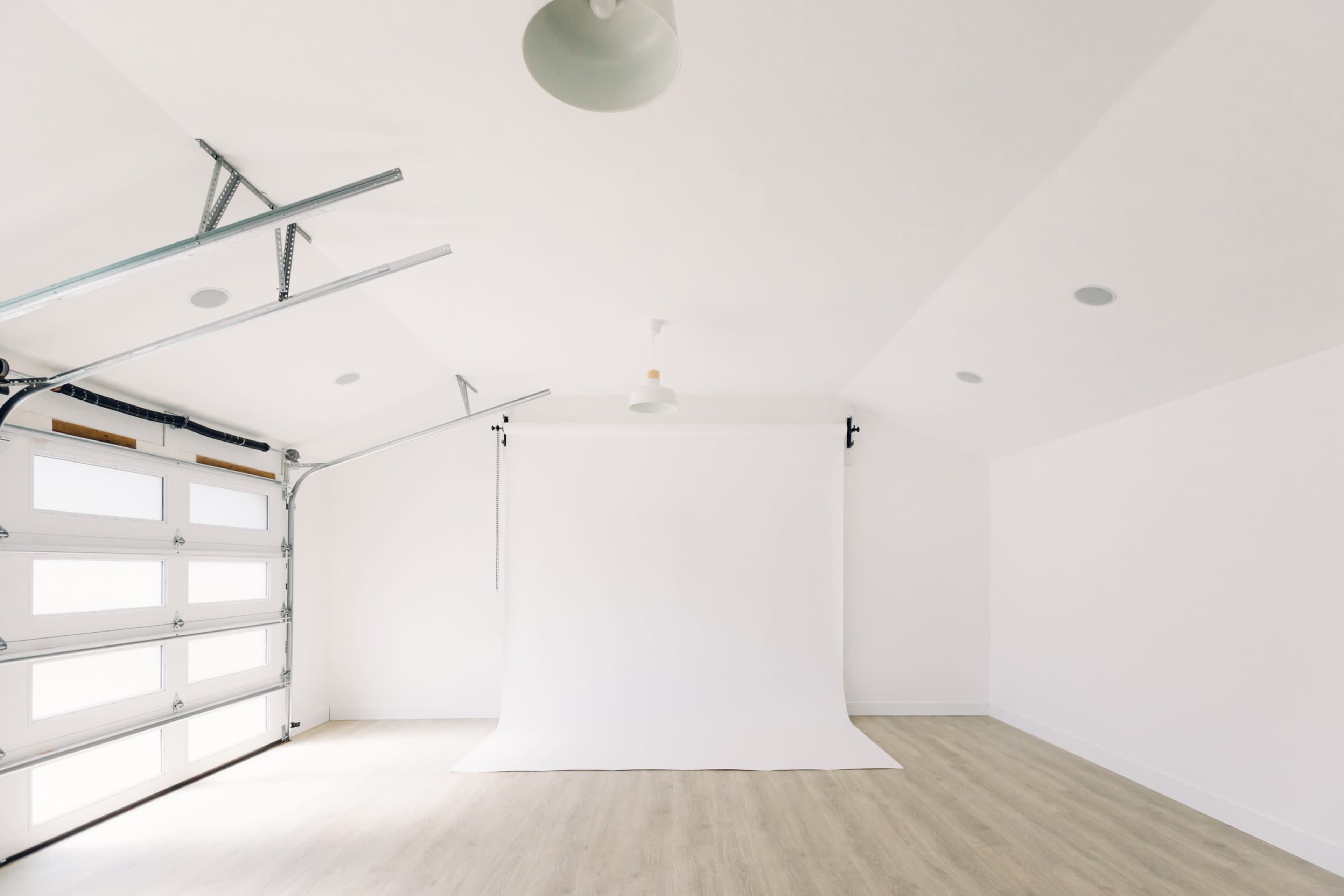 The image shows a spacious garage with a white backdrop, overhead lights, and a large garage door.