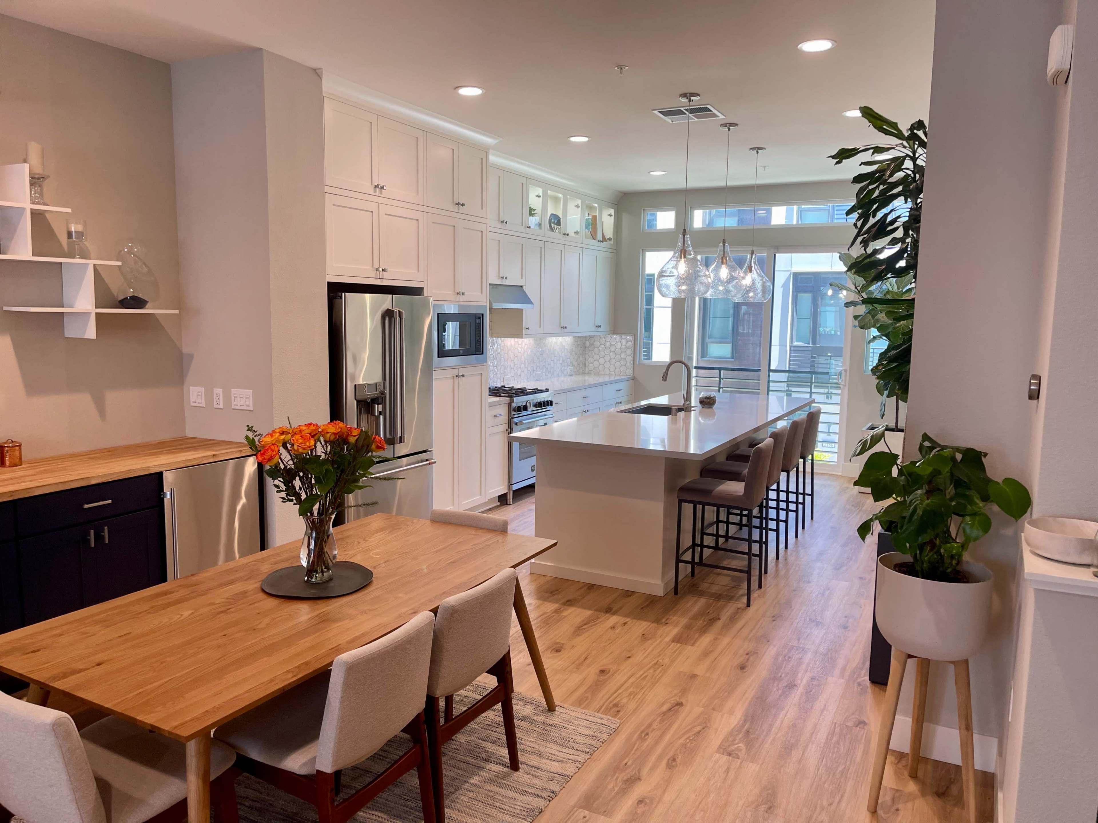 A modern kitchen and dining area with a long island, dining table, and large windows letting in natural light.