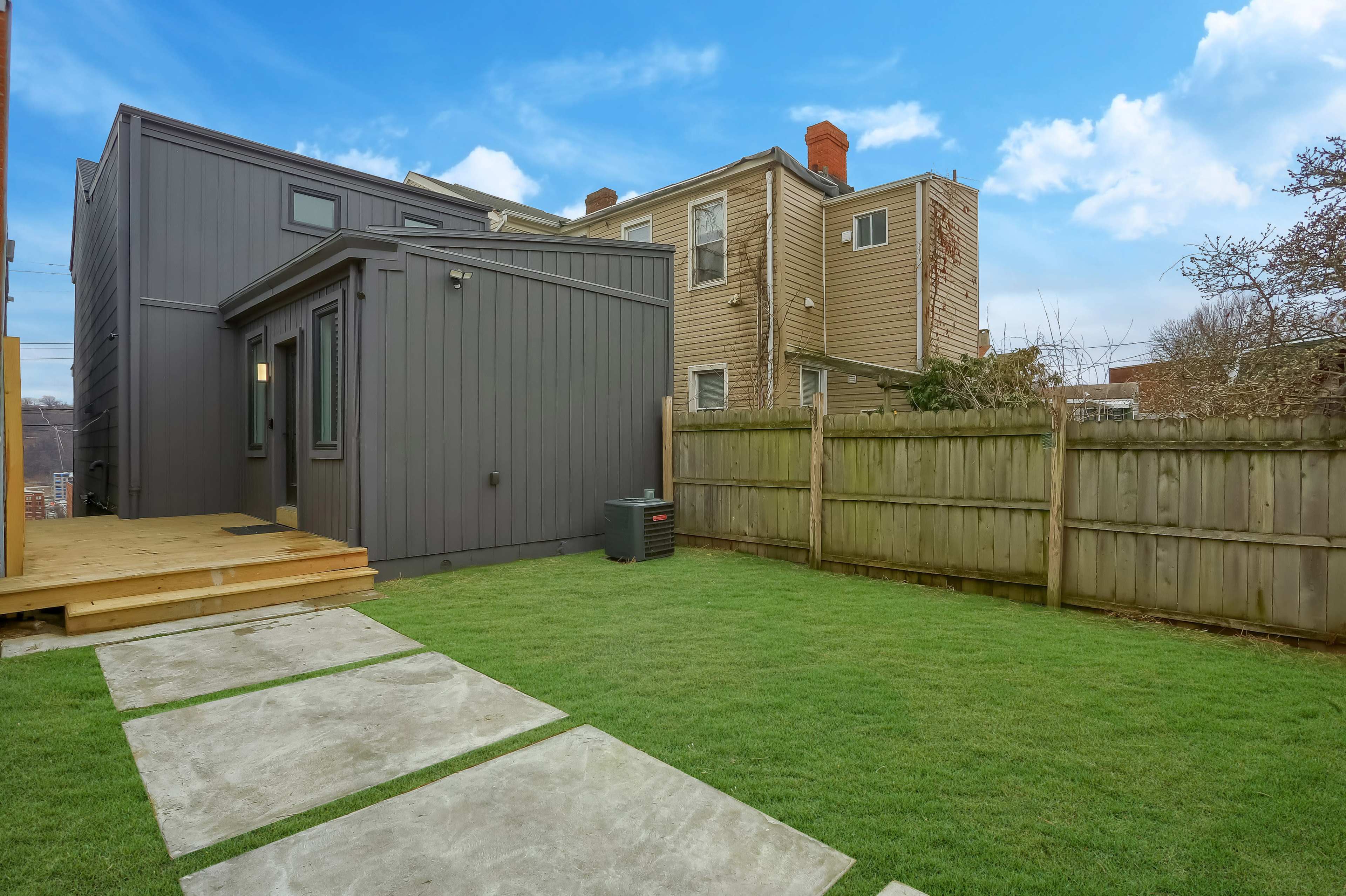 A modern house with a gray exterior, a small wooden deck, and a grassy backyard enclosed by a wooden fence.