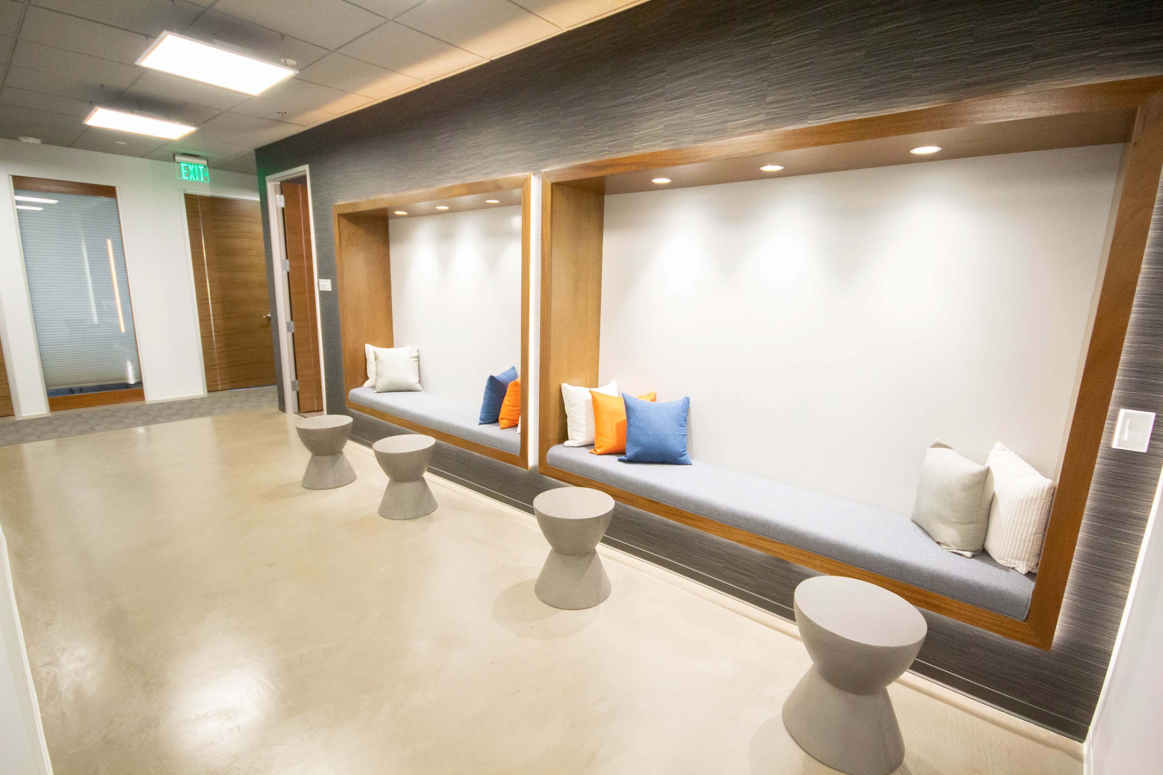 A modern hallway with two built-in seating areas, featuring cushions and small round tables.