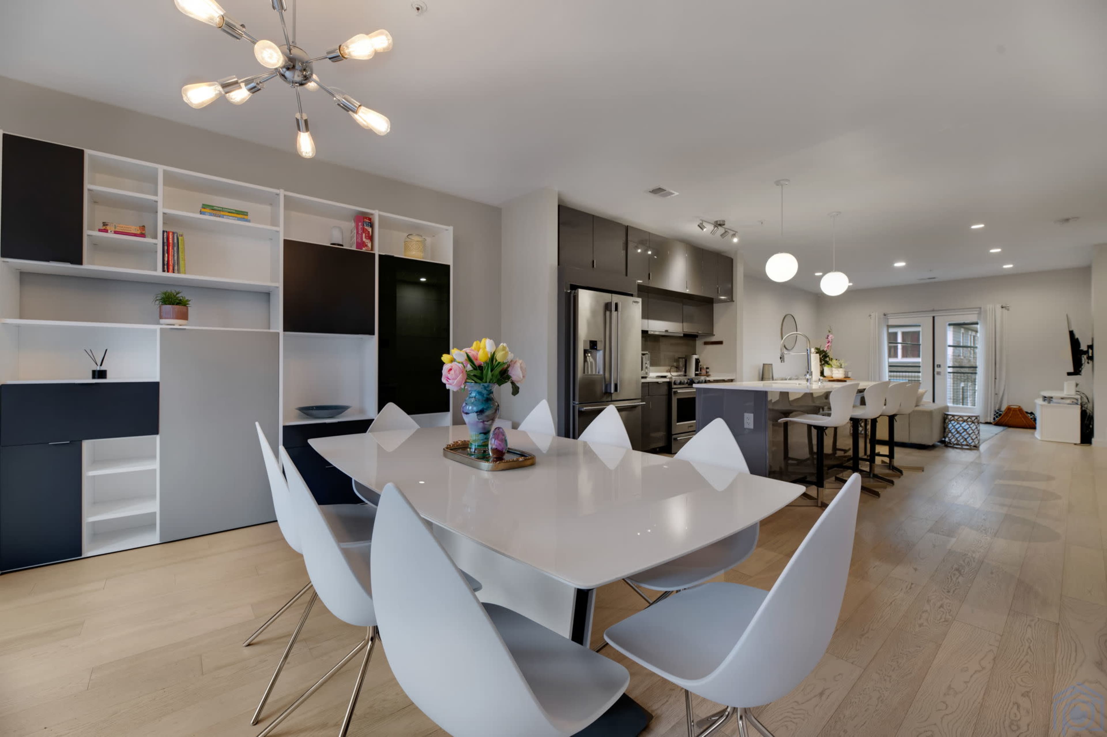 A modern dining area with a sleek white table surrounded by contemporary chairs, adjacent to a stylish kitchen featuring stainless steel appliances and a minimalist design.