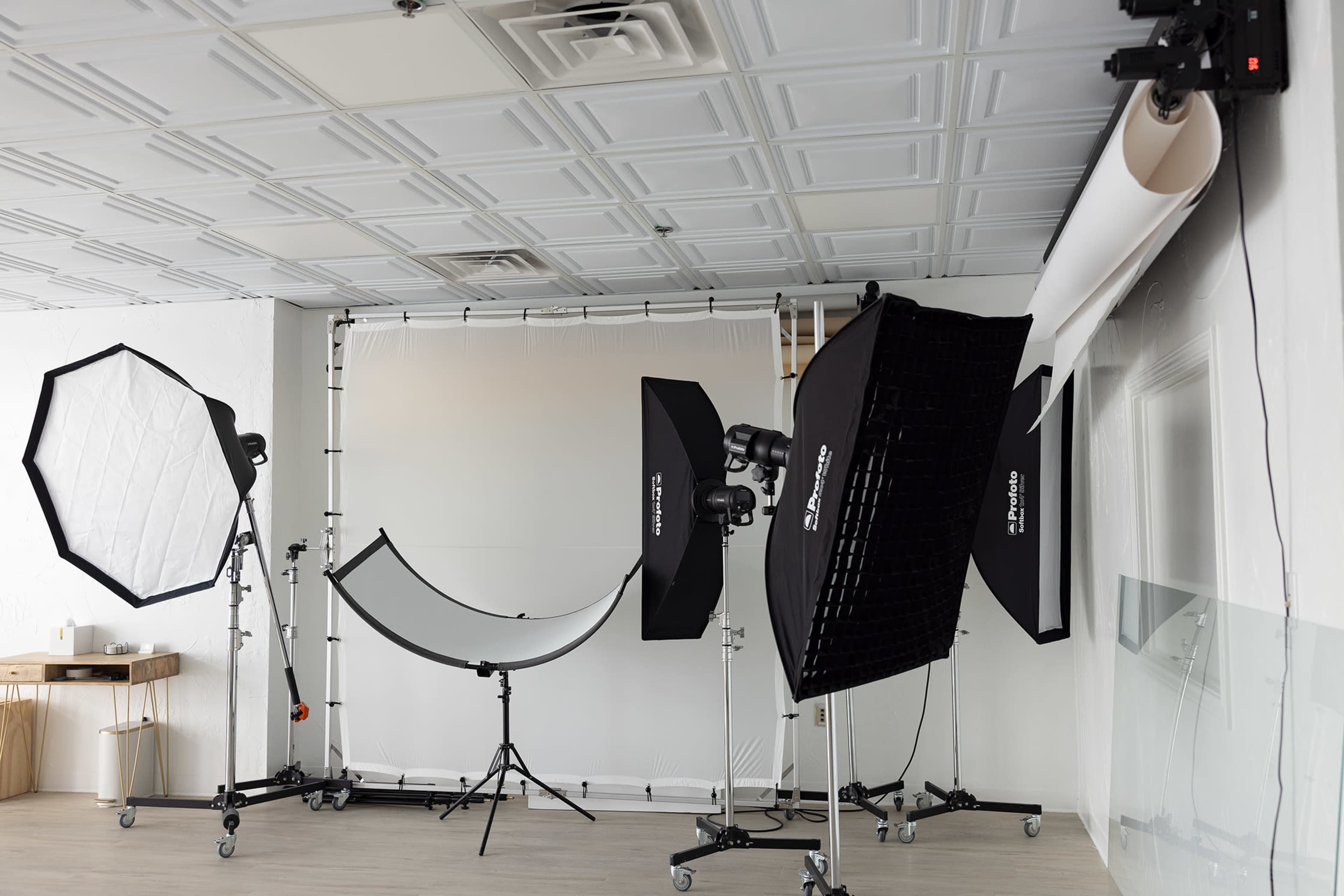 The image shows a photography studio setup with lights, softboxes, and a backdrop support system.
