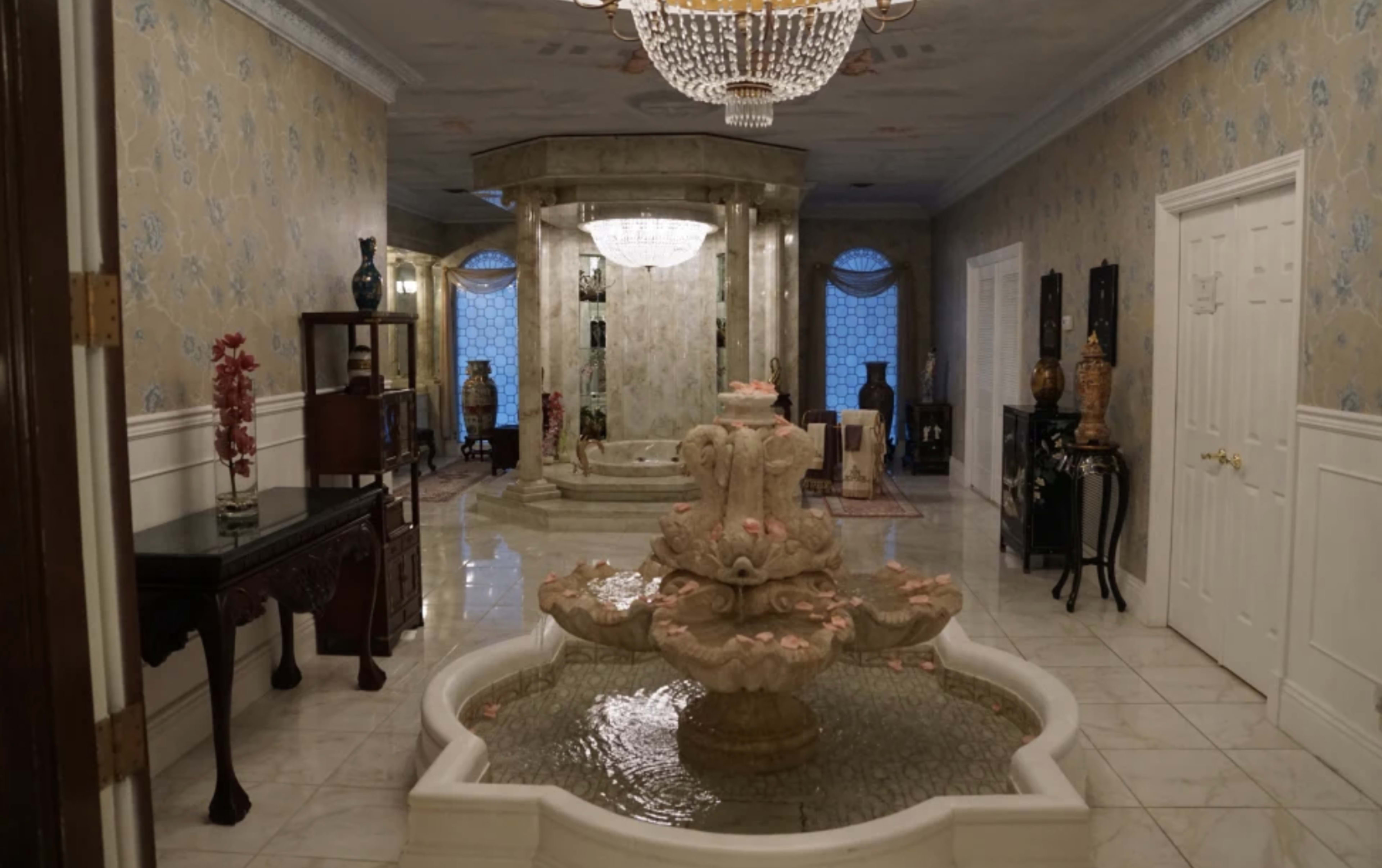 A spacious hallway with a central marble fountain, adorned with flower petals, and decorative vases lining the walls.