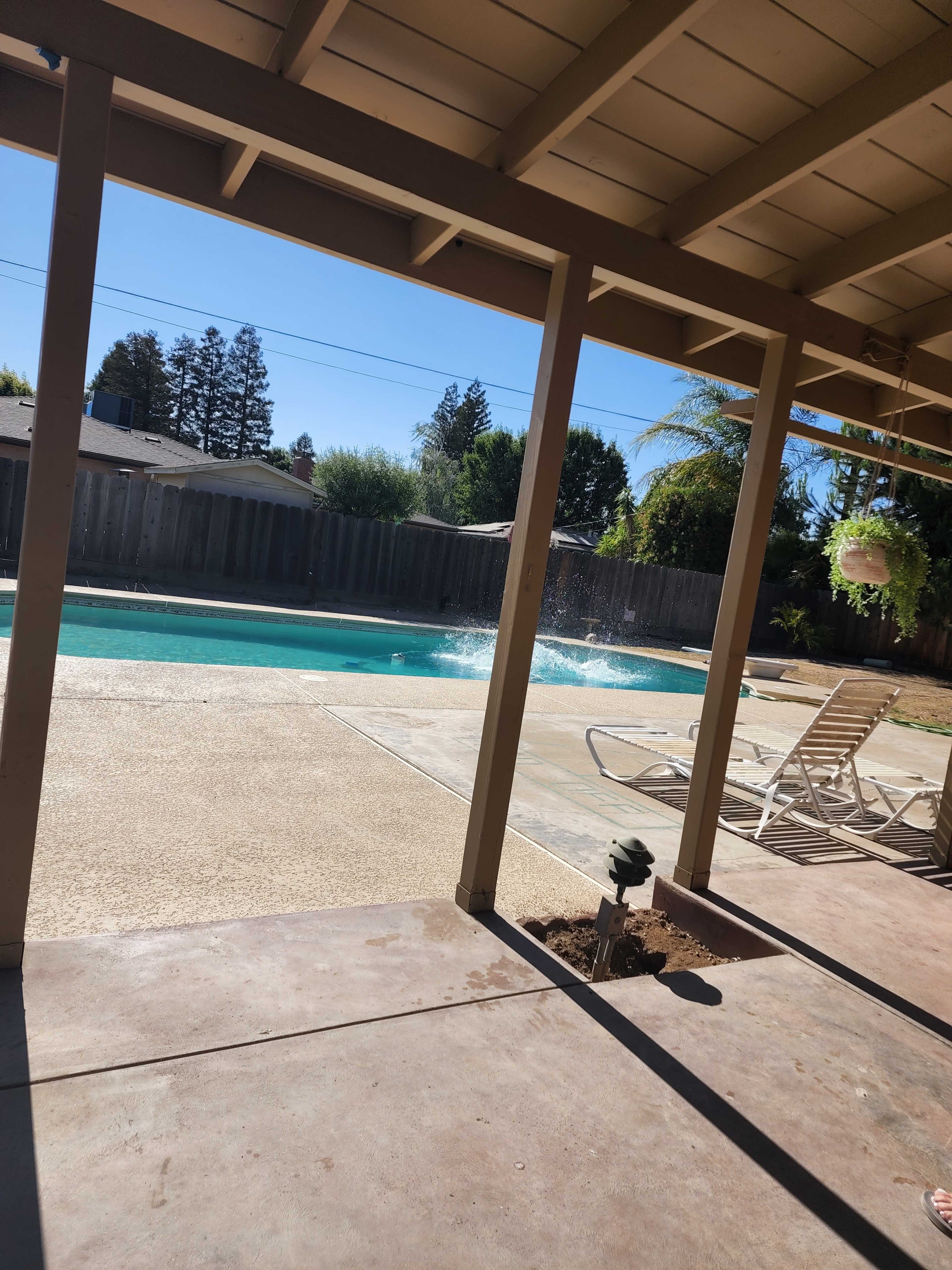 A clear swimming pool with splashes of water and a patio area with lounge chairs under a covered porch.