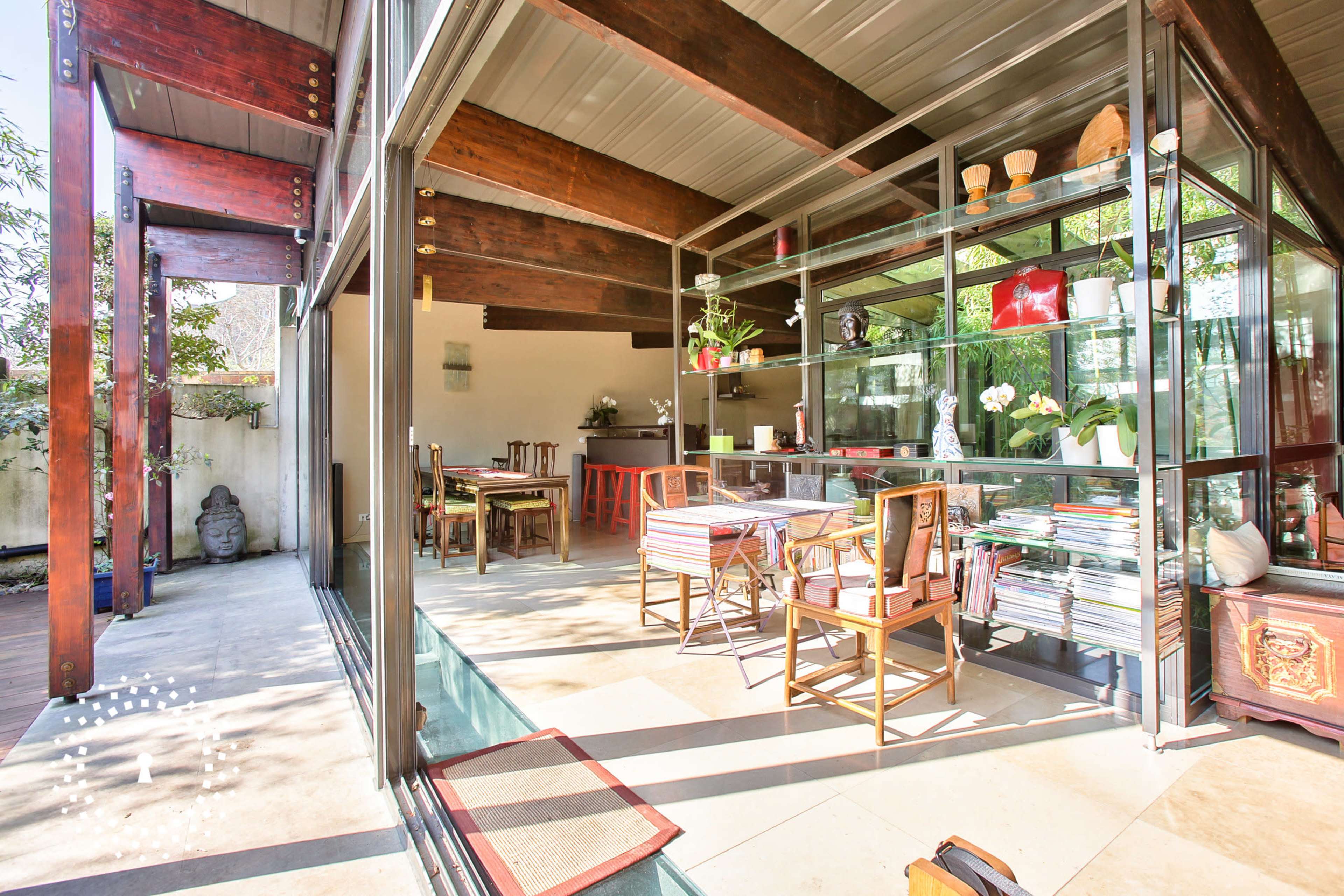 A contemporary open-concept living space with large glass walls, wooden beams, and a dining area furnished with chairs and a table.