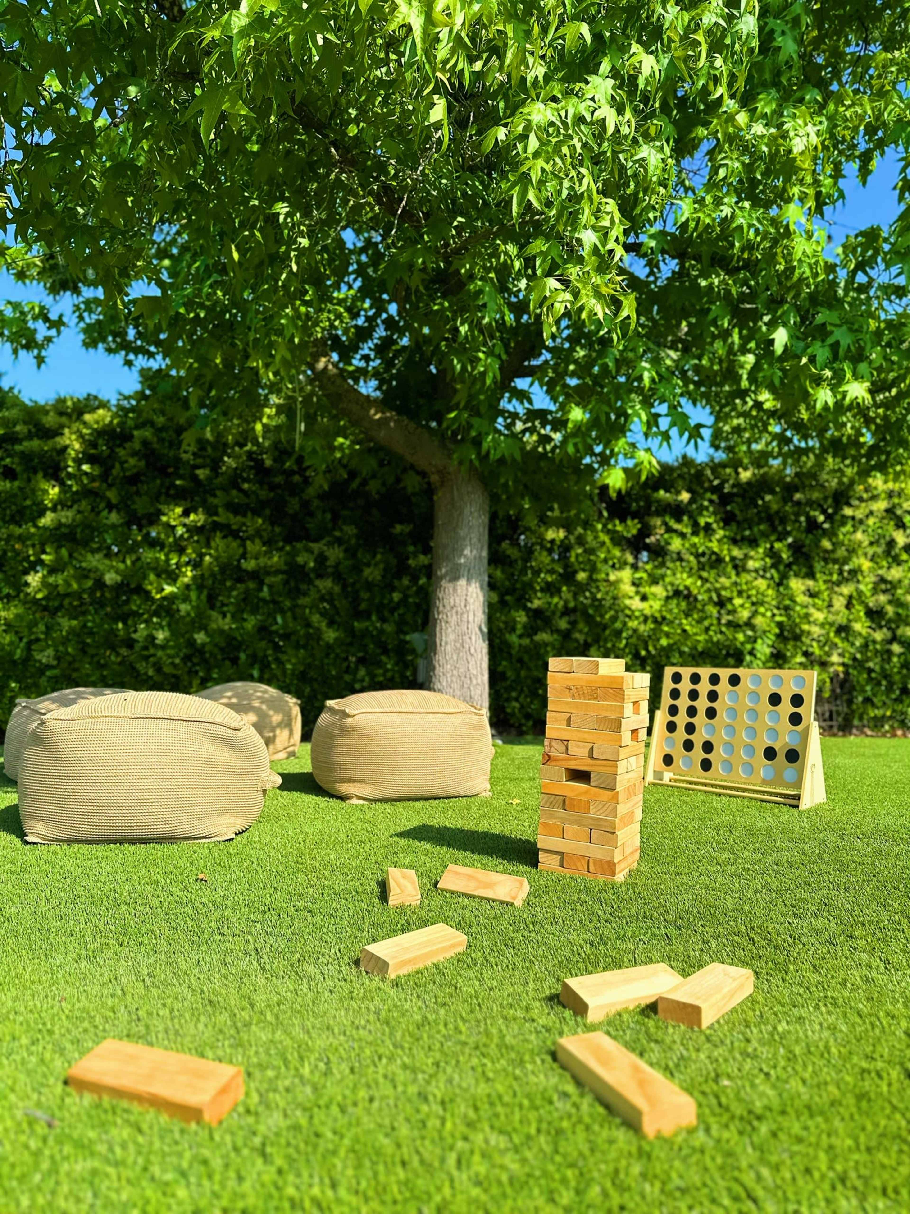 A game setup featuring a Jenga tower, Connect Four grid, and scattered wooden blocks on a green lawn under a tree.