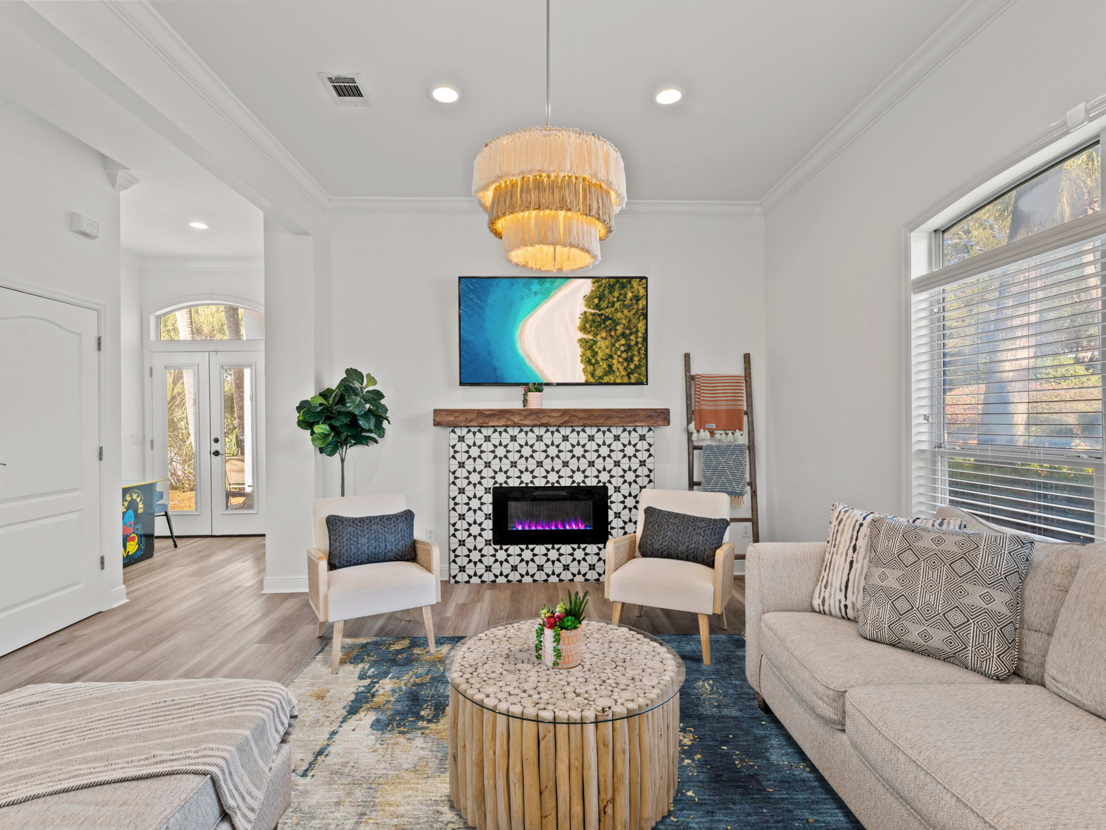 The image shows a modern living room featuring a stylish chandelier, an electric fireplace beneath a wall-mounted television, and a round coffee table made of wood.