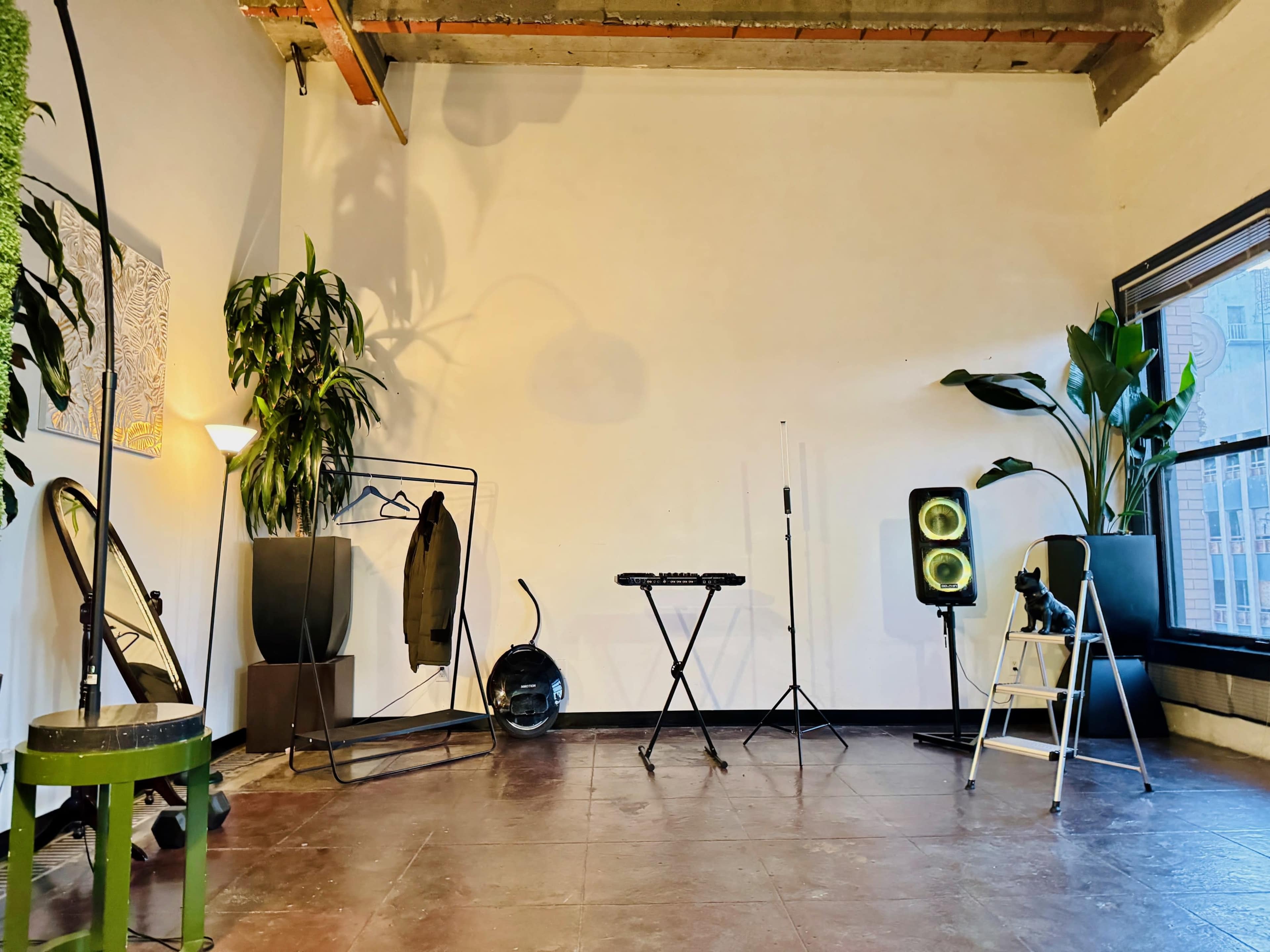 A spacious room with polished flooring, featuring plants, a clothing rack, a music stand, and various lighting equipment.