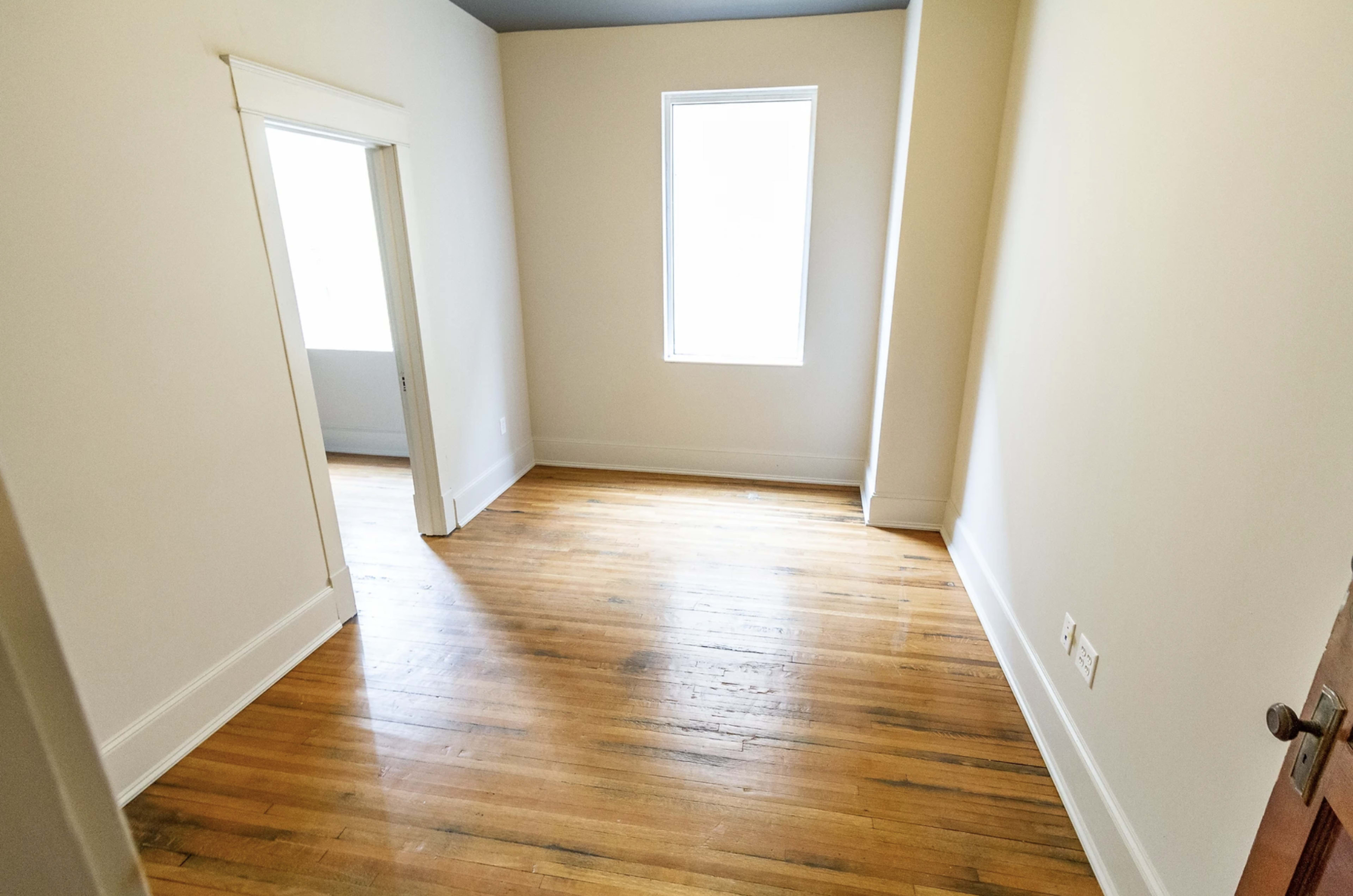 An empty room with hardwood floors, two doorways, and a large window allowing natural light.