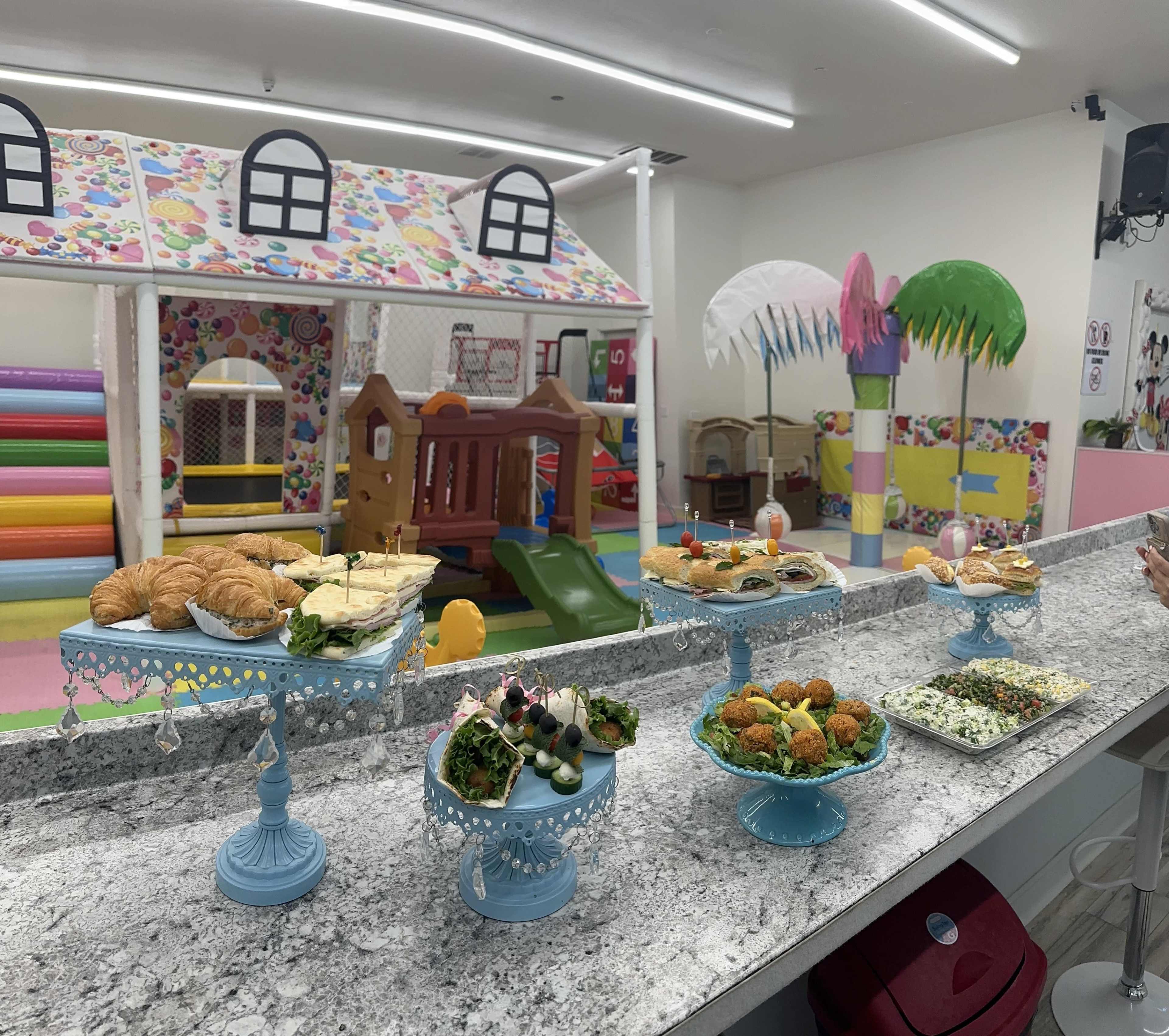 A colorful play area with a variety of dishes on decorative stands, including pastries, appetizers, and salads, arranged on a marble counter.