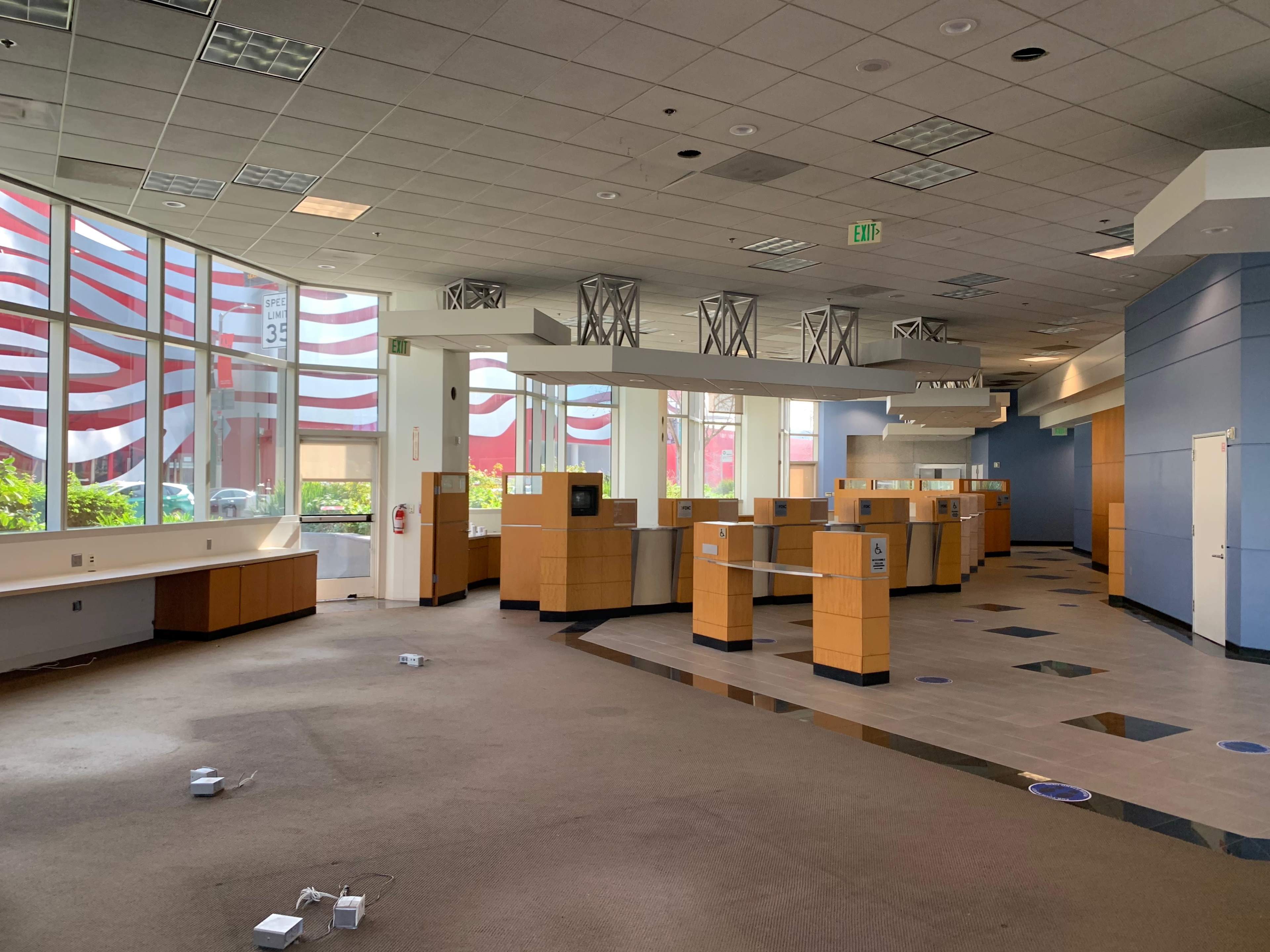 The image shows an empty, modern interior of a commercial space with wooden counters and large windows displaying red and white decorations outside.