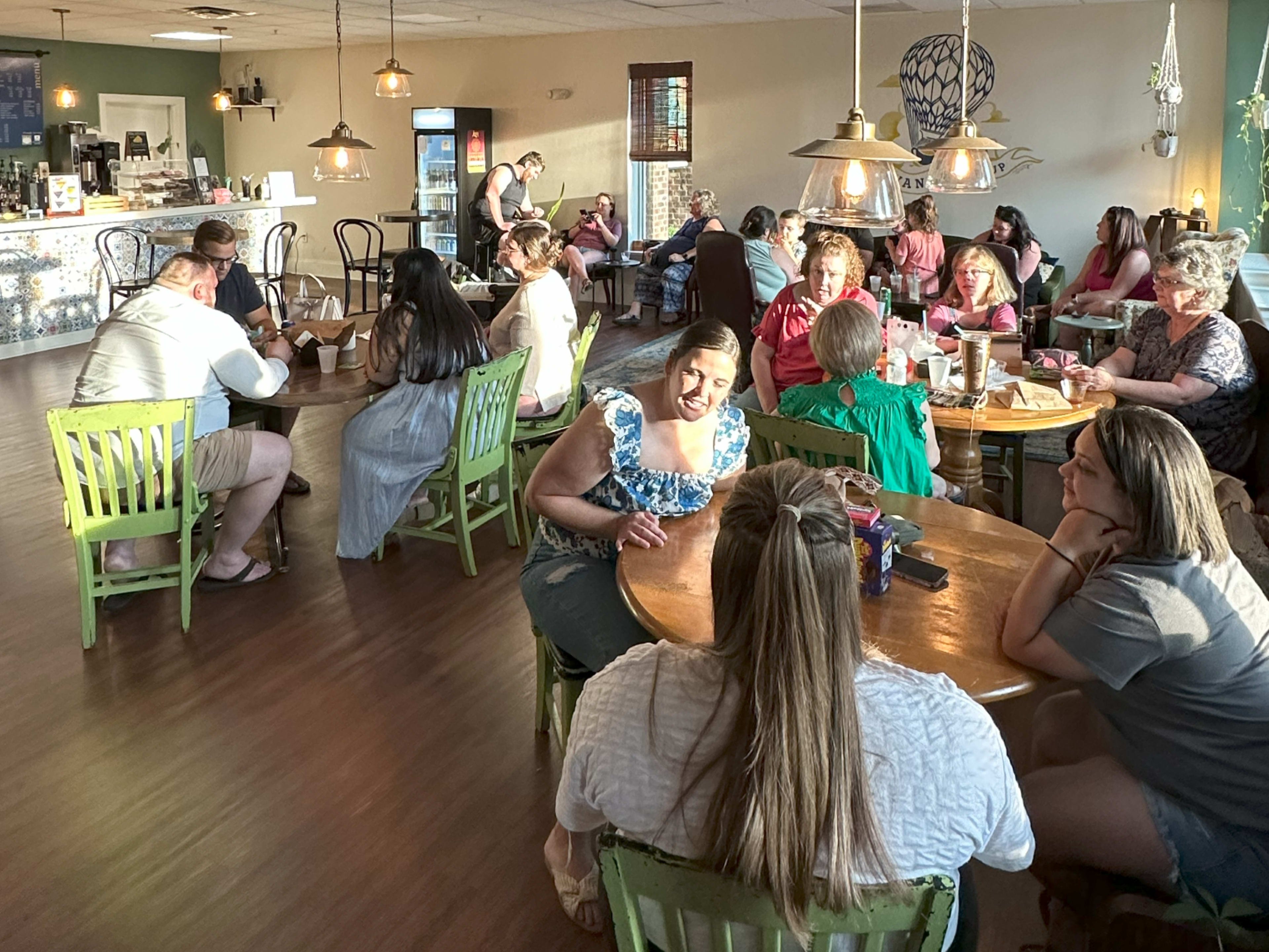 A busy café filled with patrons sitting at wooden tables, engaged in conversation and enjoying their drinks.
