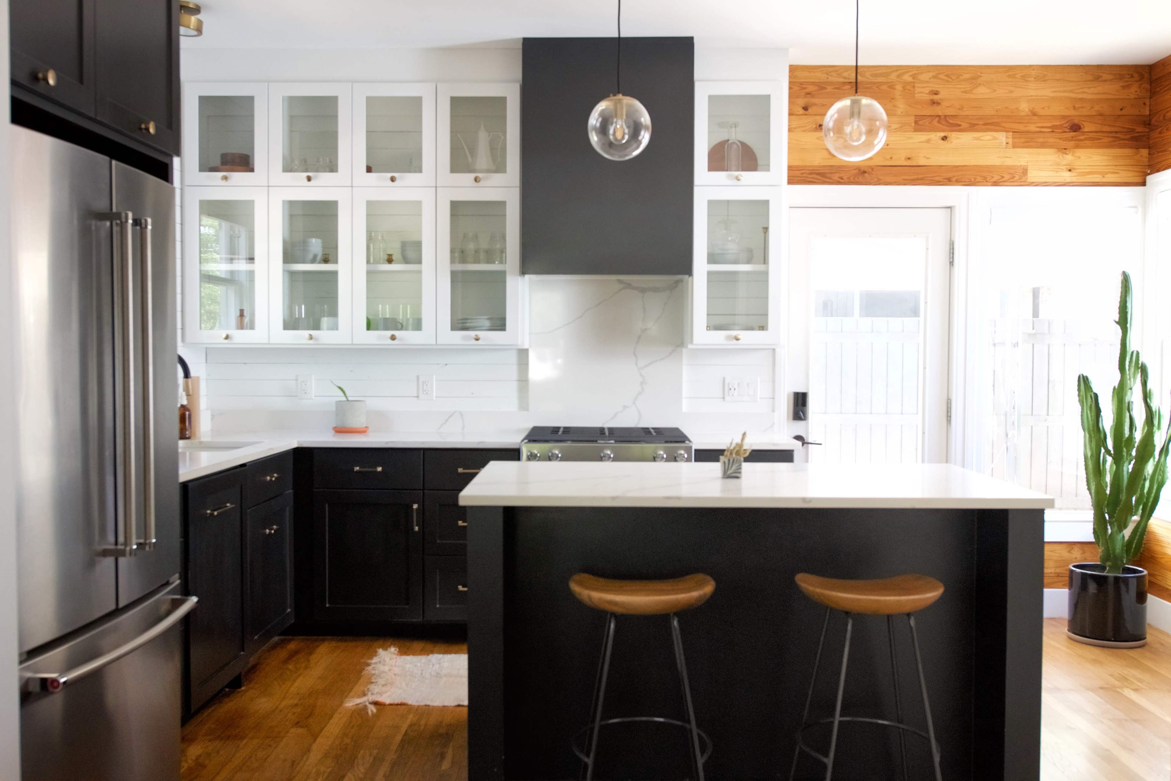 A modern kitchen features dark cabinetry, a central island with two stools, and large windows allowing natural light.