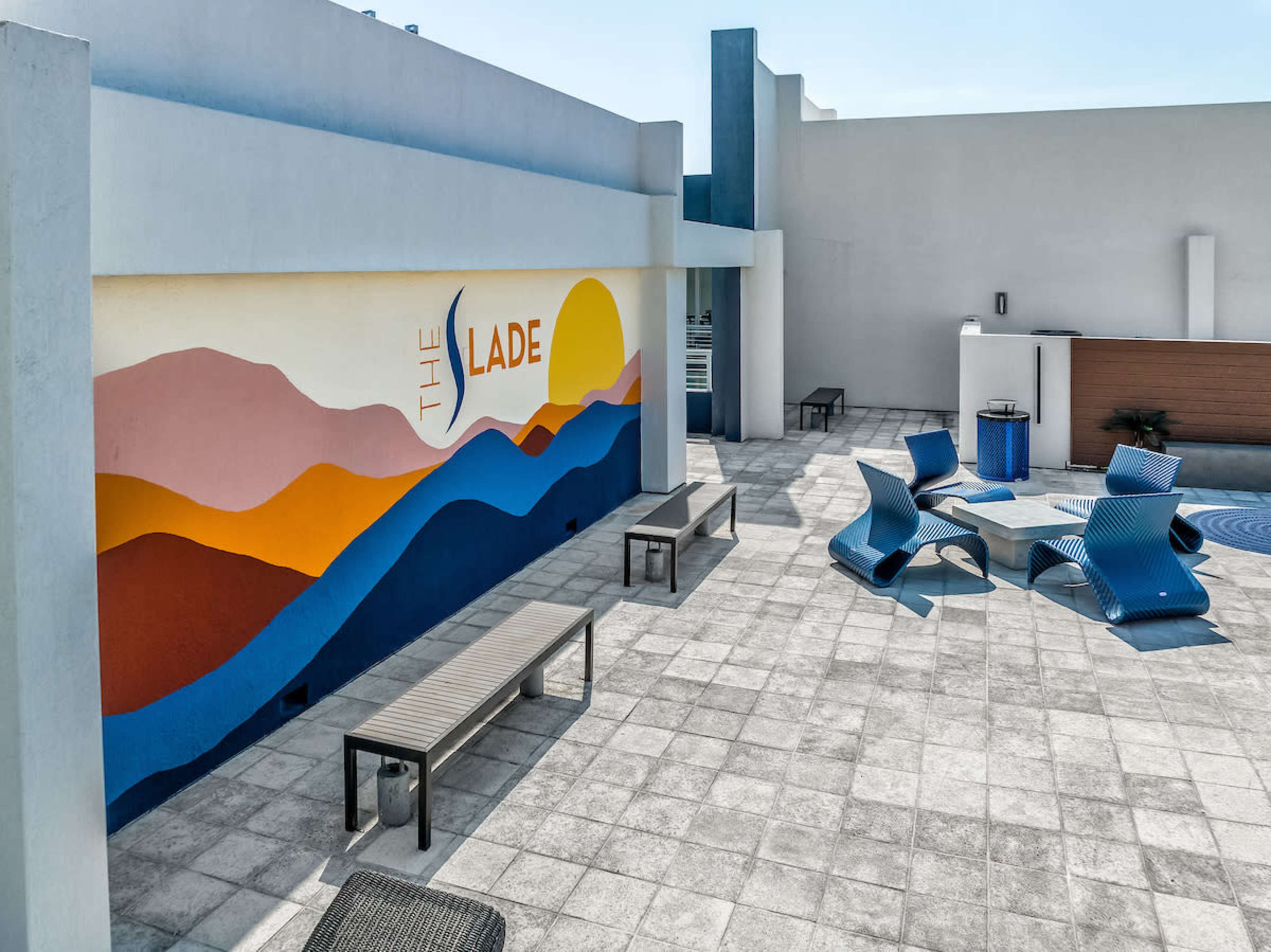 A rooftop area featuring a colorful mural with mountains and a sun, complemented by modern outdoor seating arrangements on tiled flooring.