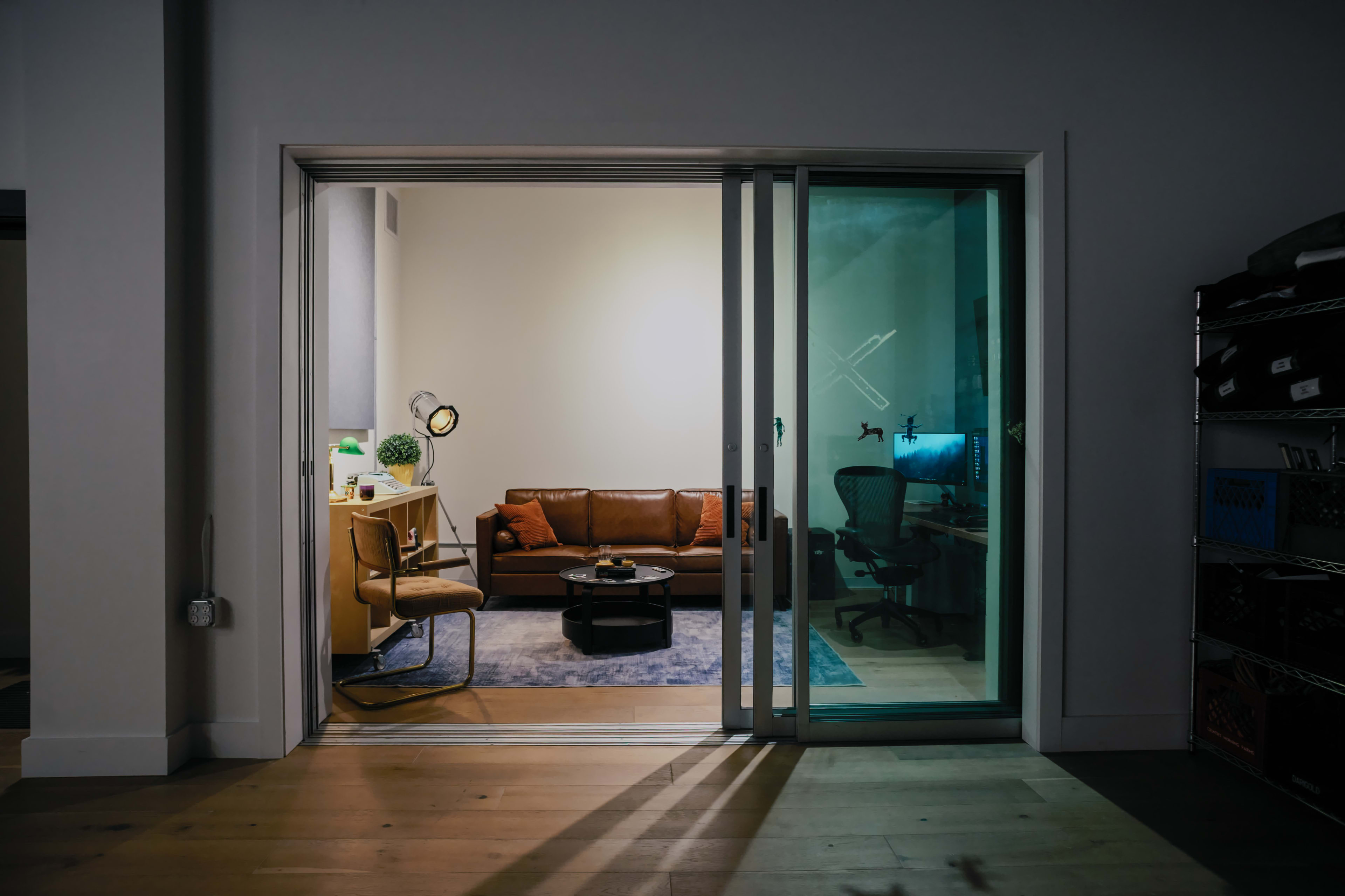A modern room features a leather sofa, a desk with a chair, and a large sliding glass door leading to an outdoor area.