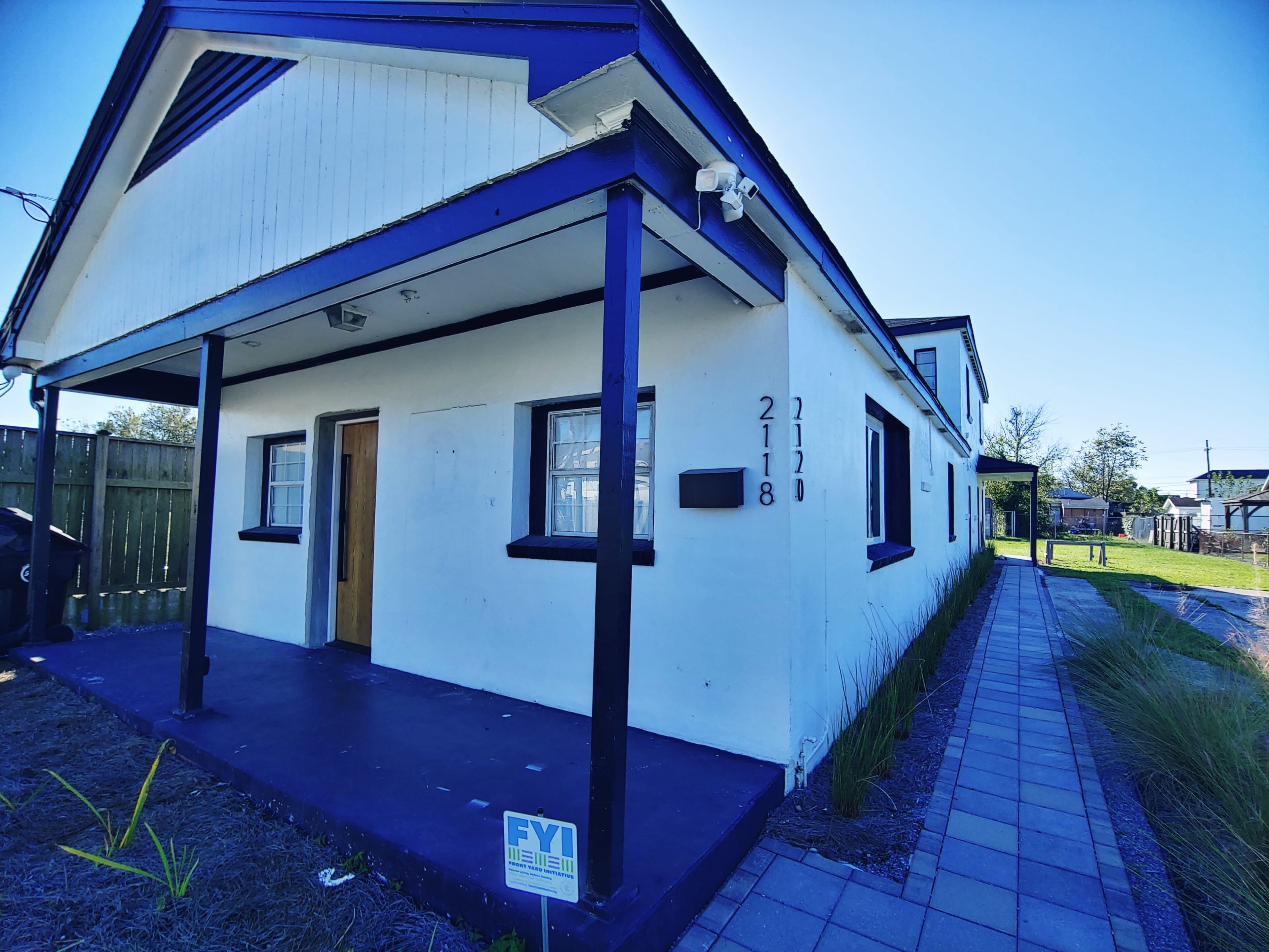 The image shows a white building with blue accents, featuring two doorways labeled 2118 and 2120, and a paved walkway leading to the entrance.