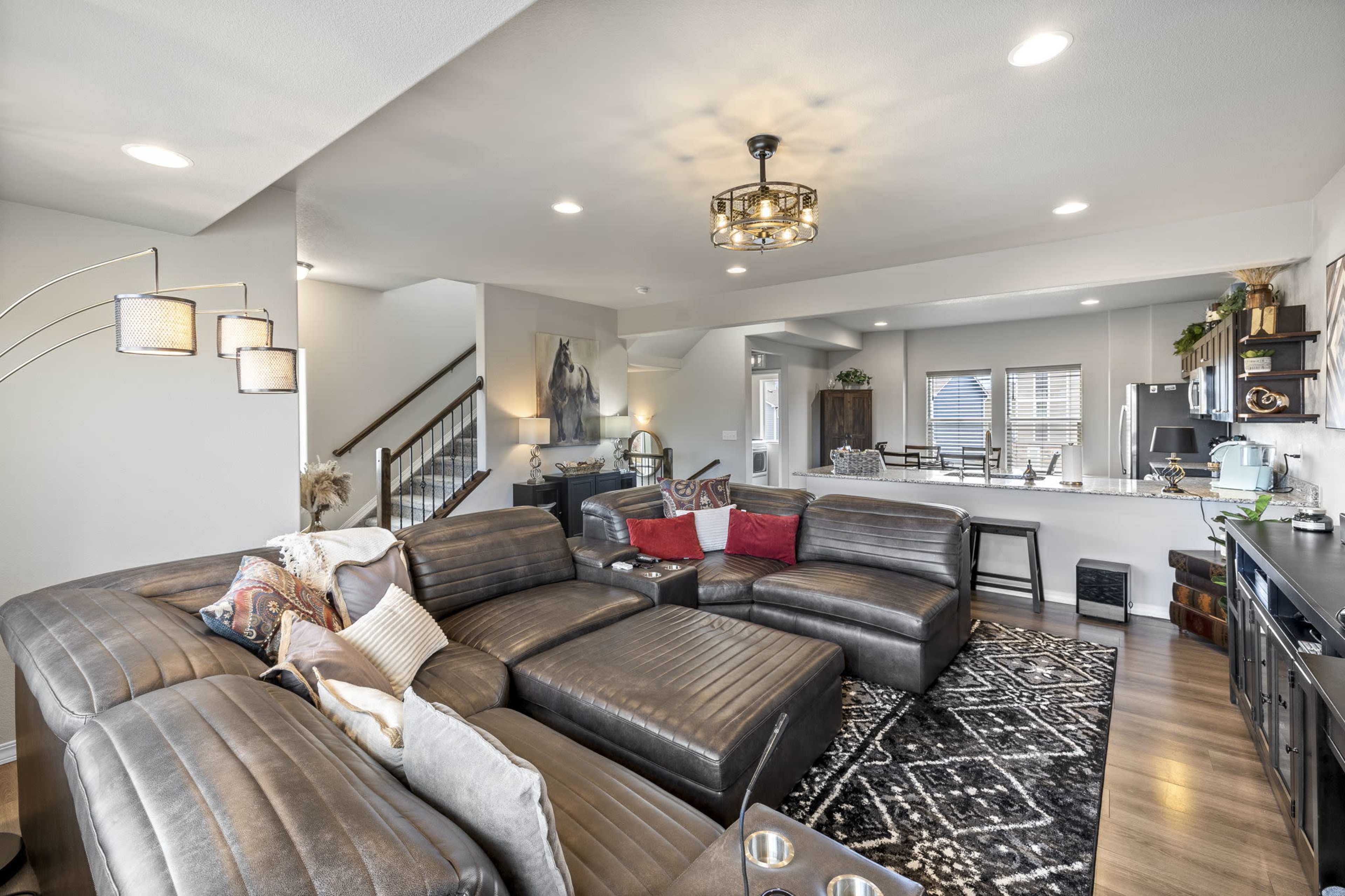 A modern living room featuring a large sectional sofa, a coffee table, and a view into a dining area with a kitchen in the background.